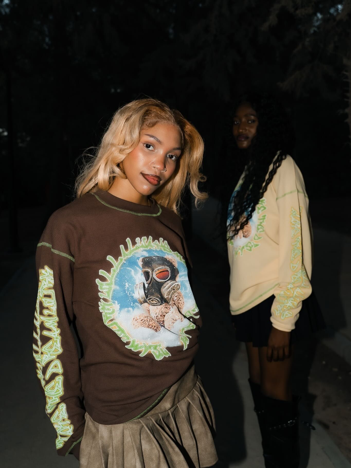 Two people wearing graphic brown and cream long sleeve shirts outdoors at night in a dark setting.