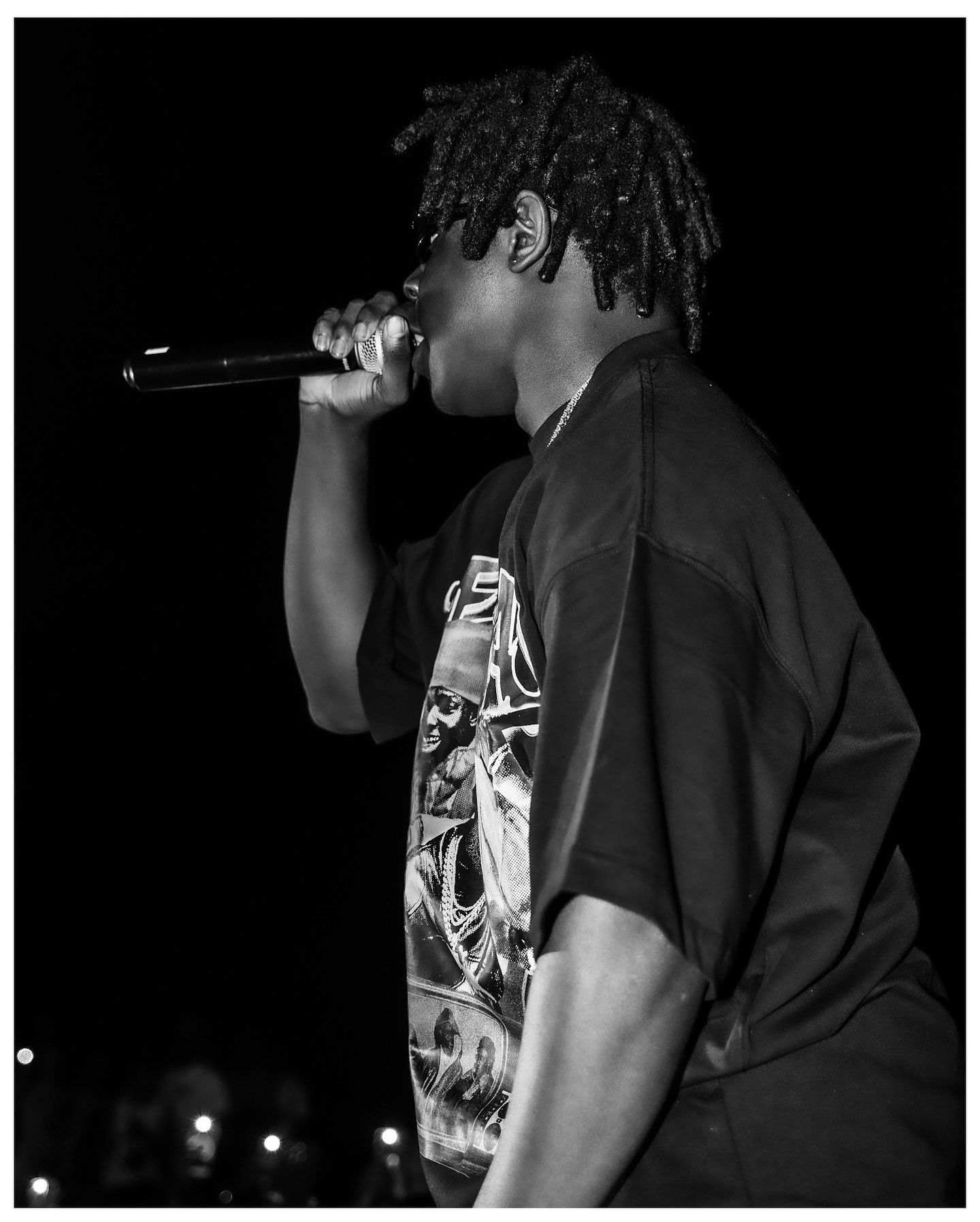 Black and white photo of a young male rapper performing on stage, holding a microphone close to his mouth.
