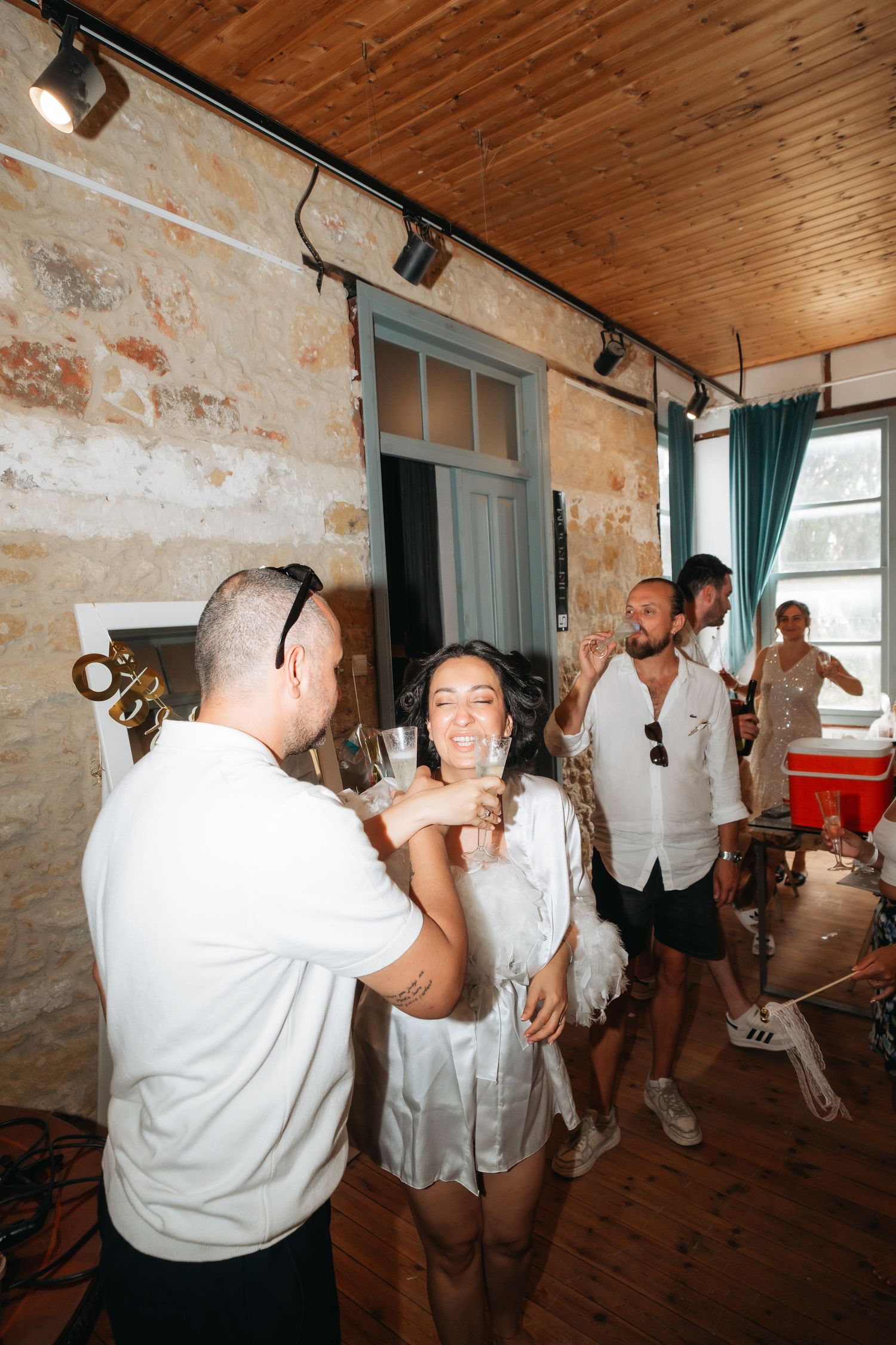 Group of friends enjoying drinks and dancing at an indoor party in a rustic stone-walled venue with wooden ceiling.