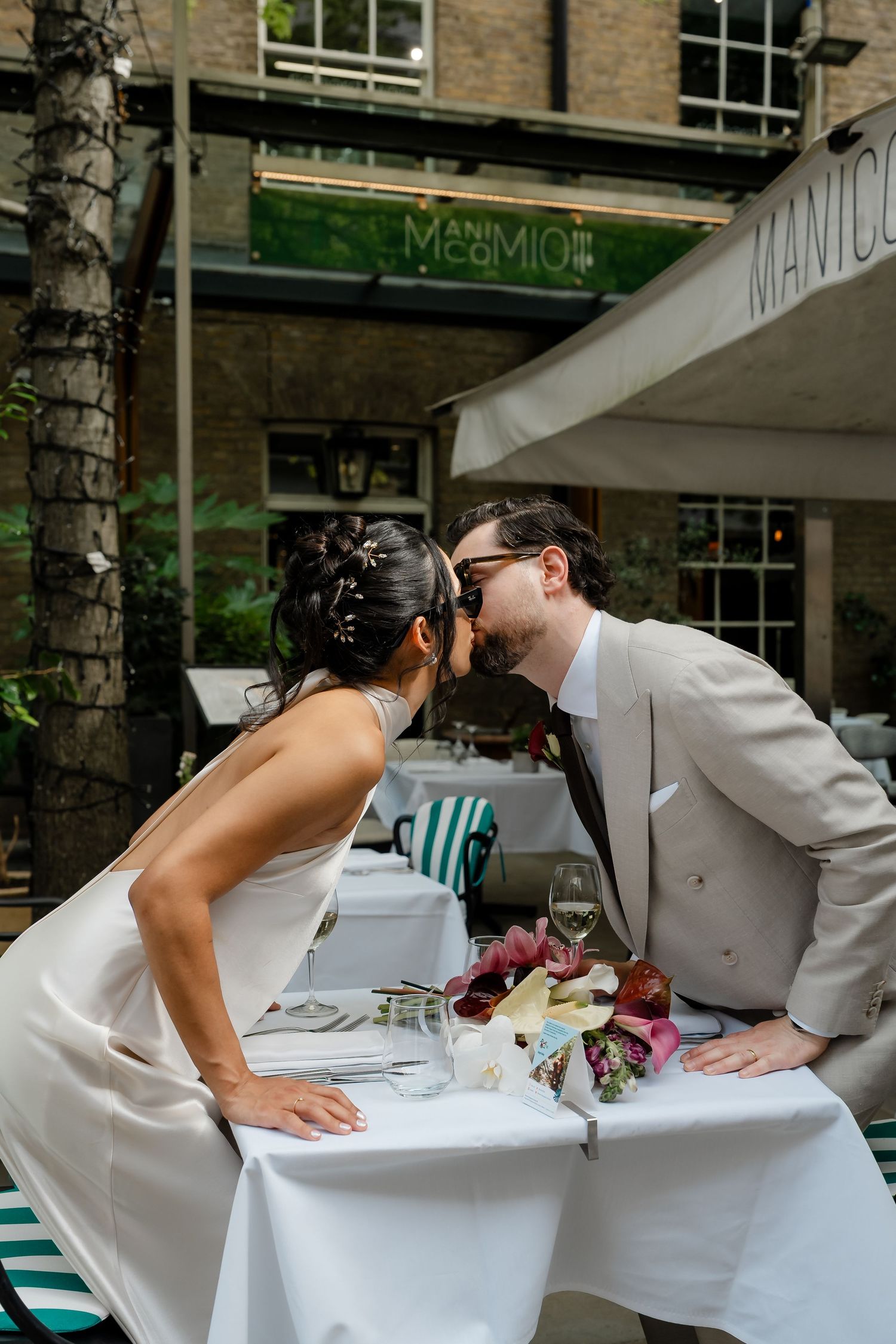 Bride and groom sharing a kiss across table at Manico restaurant wedding.