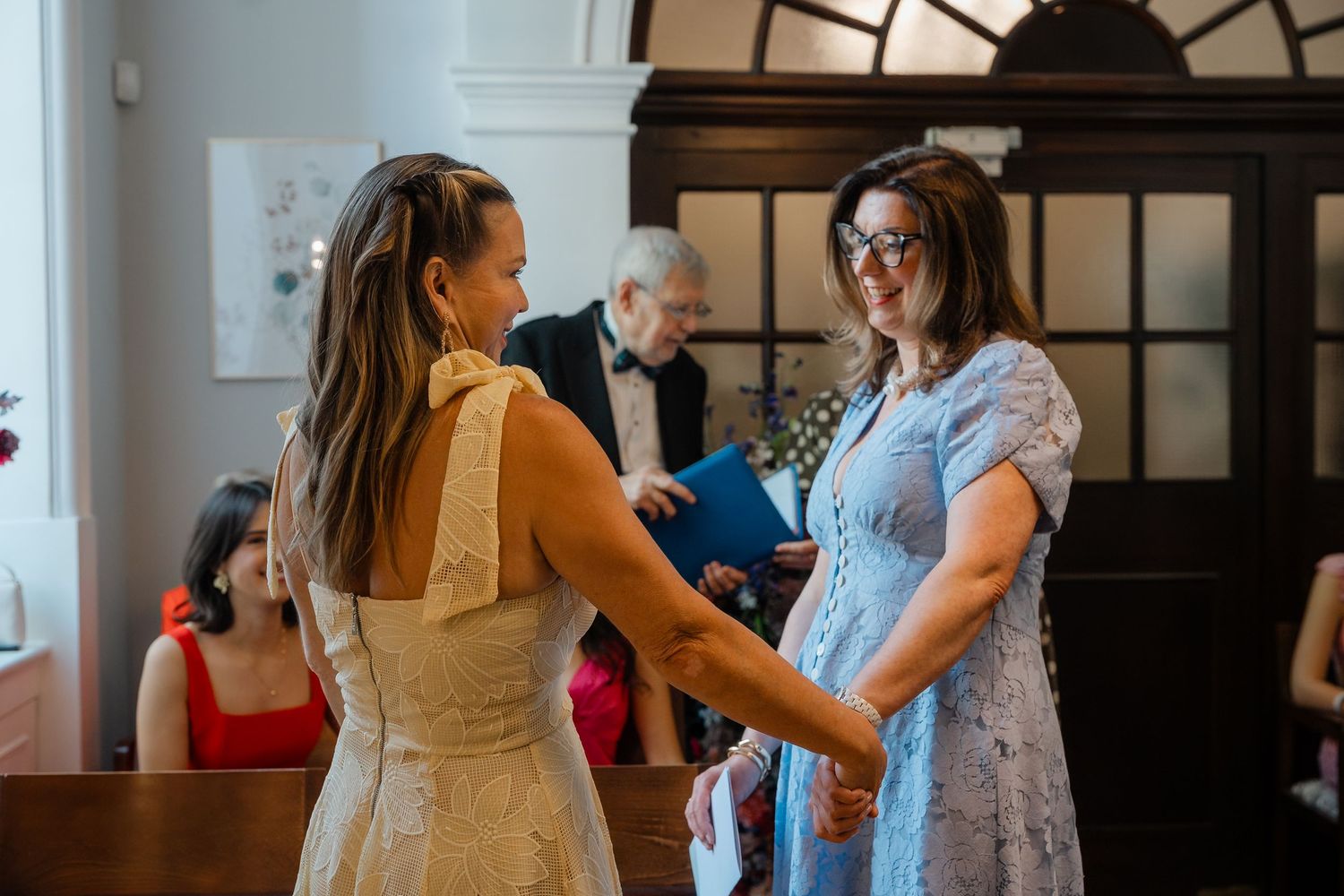 Two women holding hands during an intimate indoor wedding ceremony.