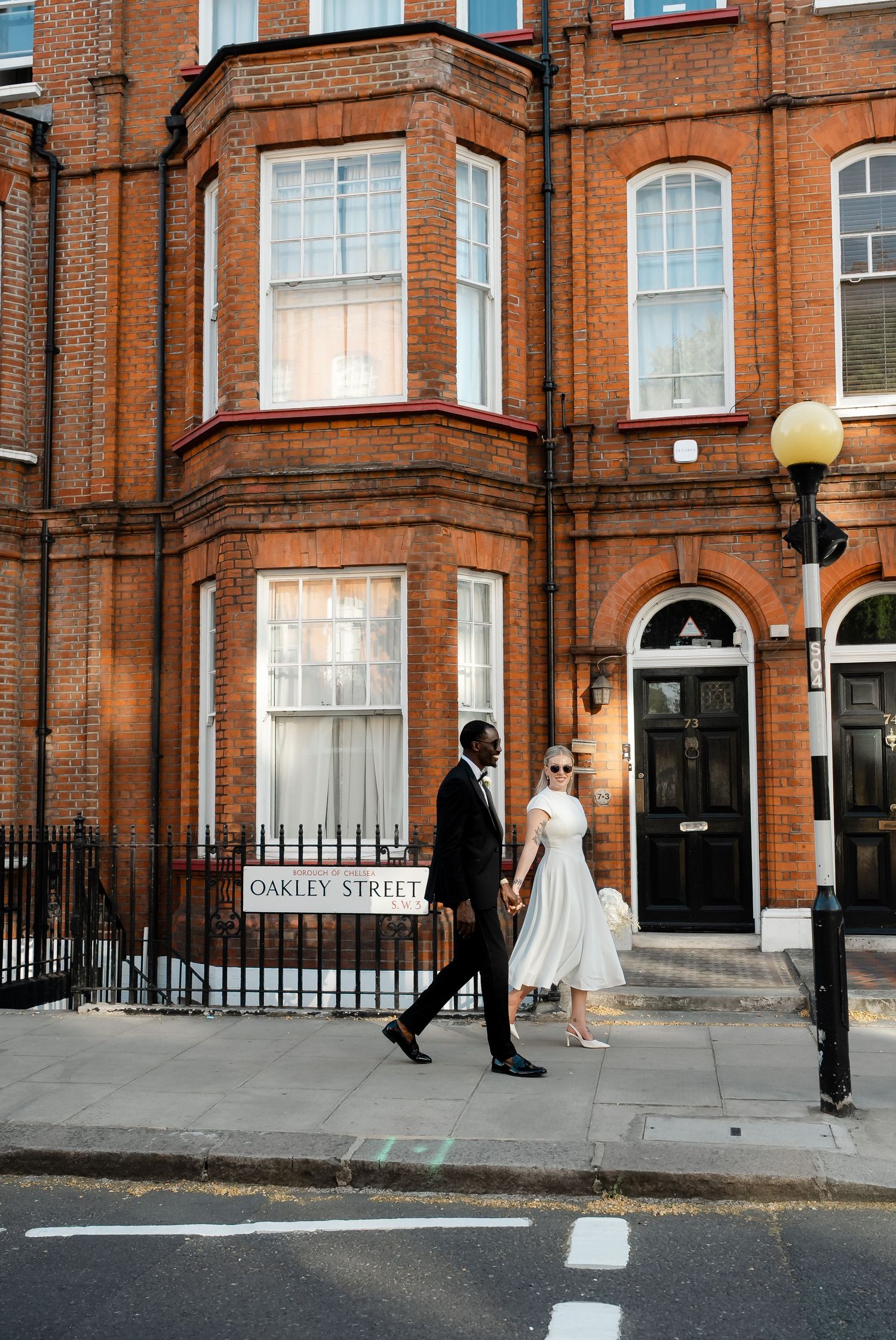 Elegant couple walking hand in hand past a red brick building on Oakley Street London.