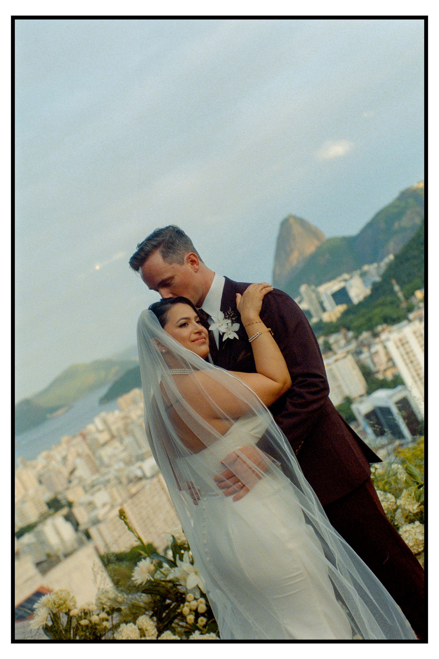Bride and groom embracing romantically with Rio de Janeiro skyline and Sugarloaf Mountain backdrop.