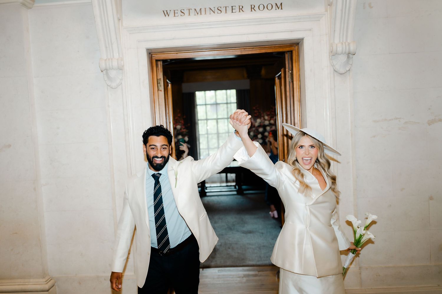 Newlywed couple celebrating exit from Westminster Room raising hands in triumph.