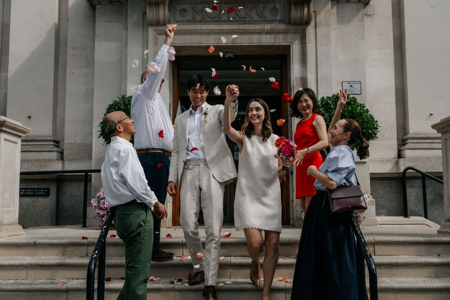 Joyful newlyweds celebrating with confetti on steps surrounded by family after ceremony.