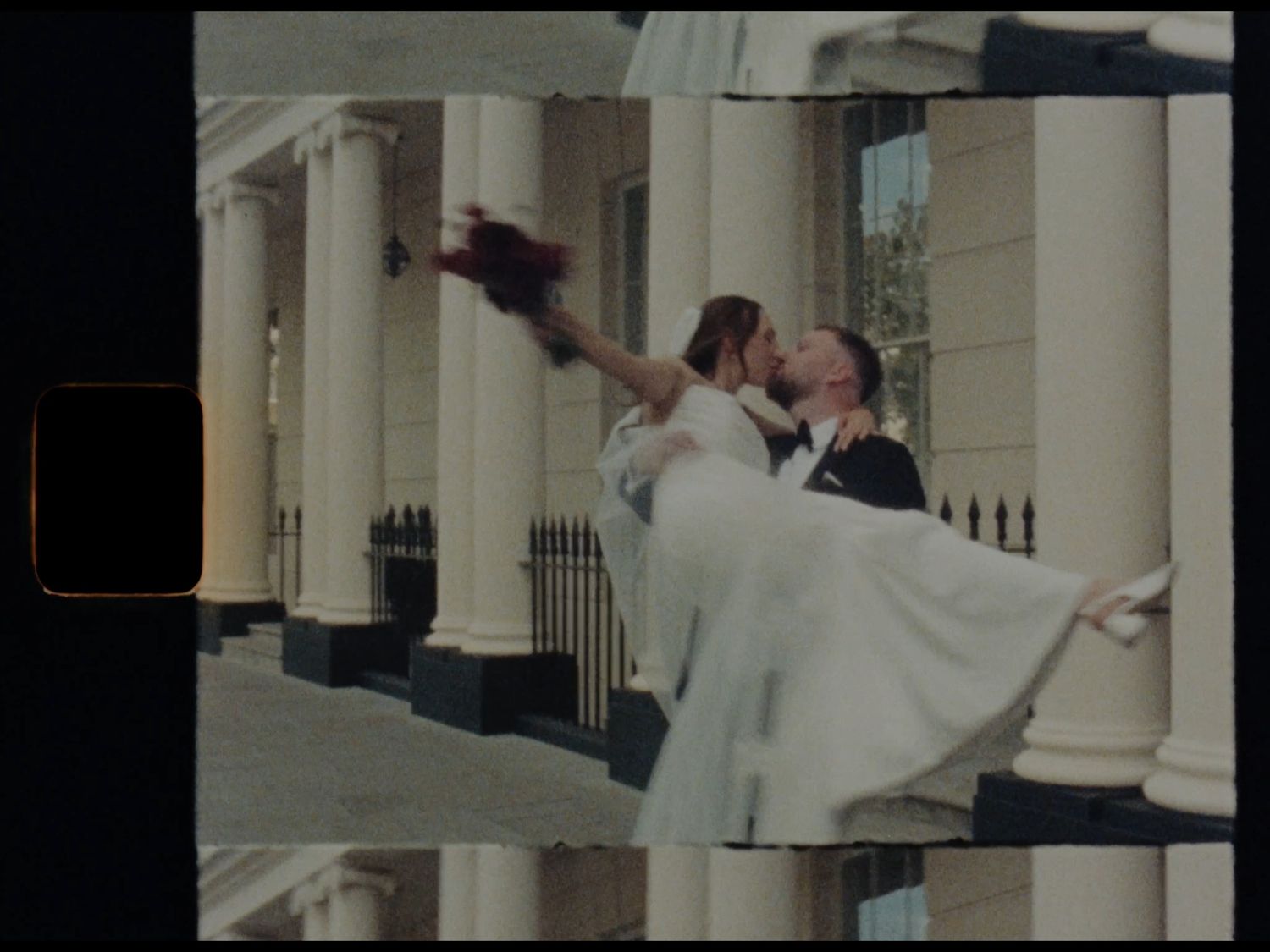A groom lifts his bride outside a grand white columned building in a joyful wedding photo.