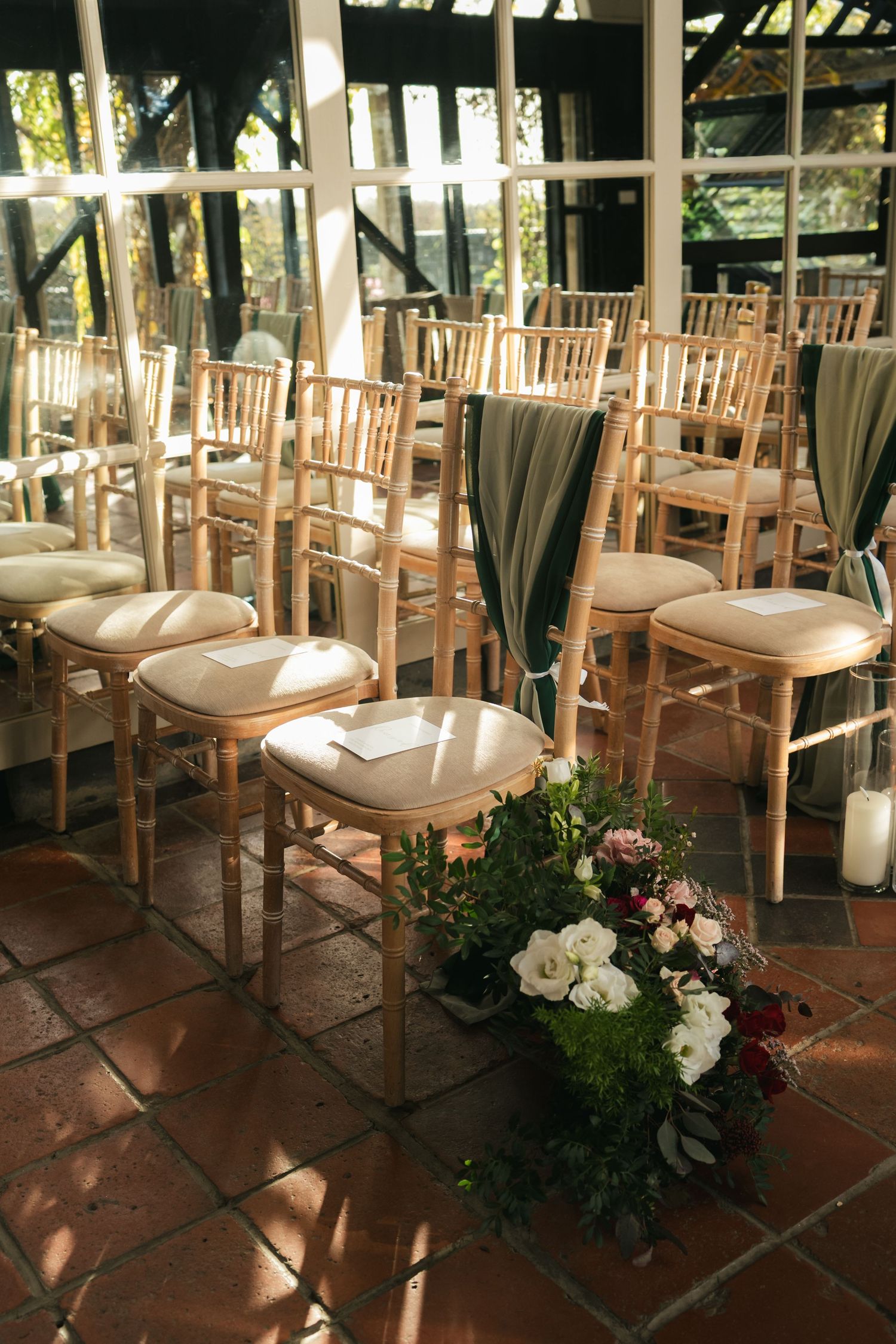 Elegant wedding ceremony setup with gold chiavari chairs, green sashes, and floral arrangements in a greenhouse venue.