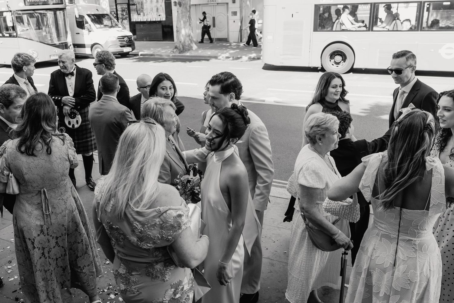 Newlyweds greeting wedding guests on busy street in black and white photo.
