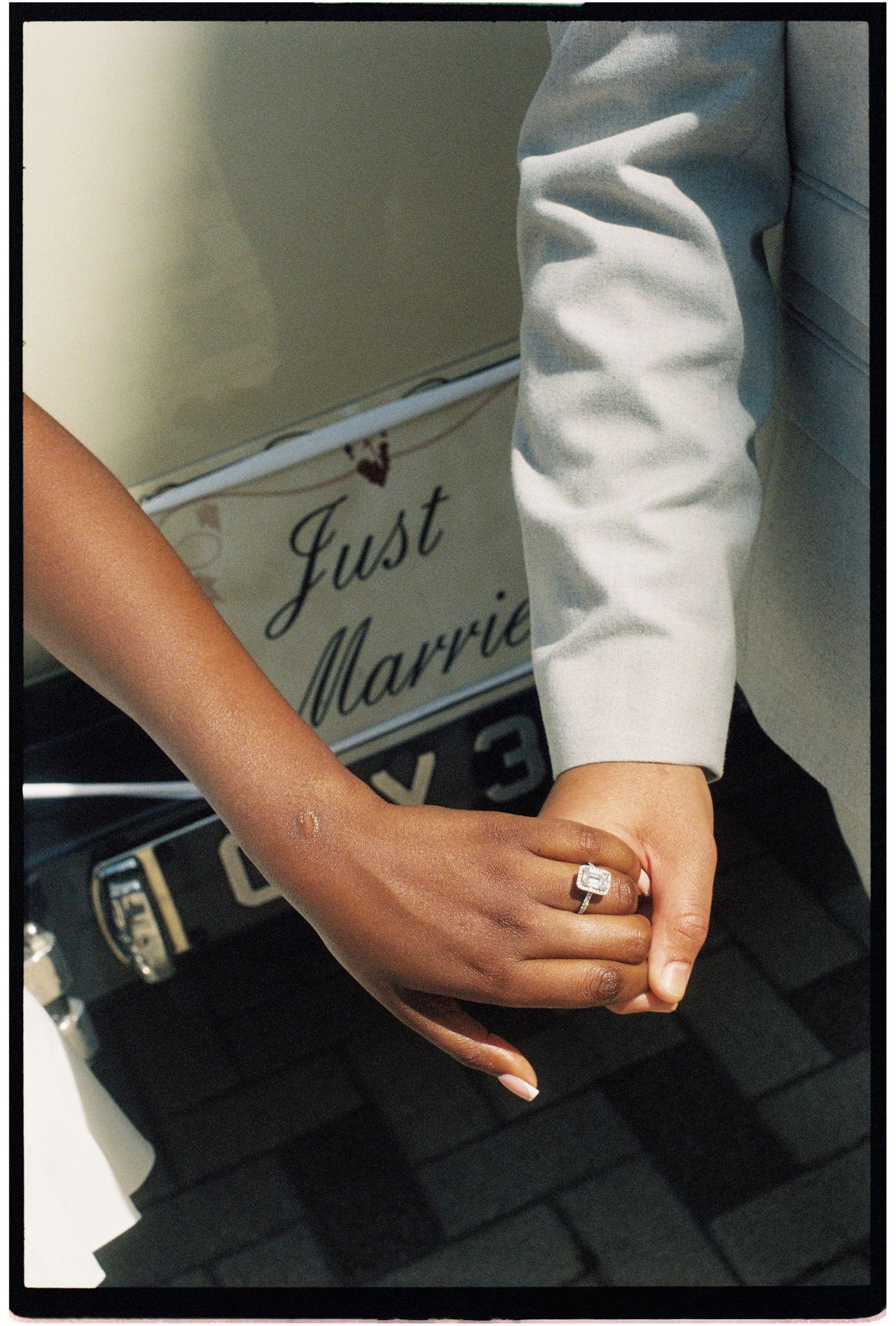 Newlyweds hold hands near a Just Married sign, bride wearing a diamond engagement ring.