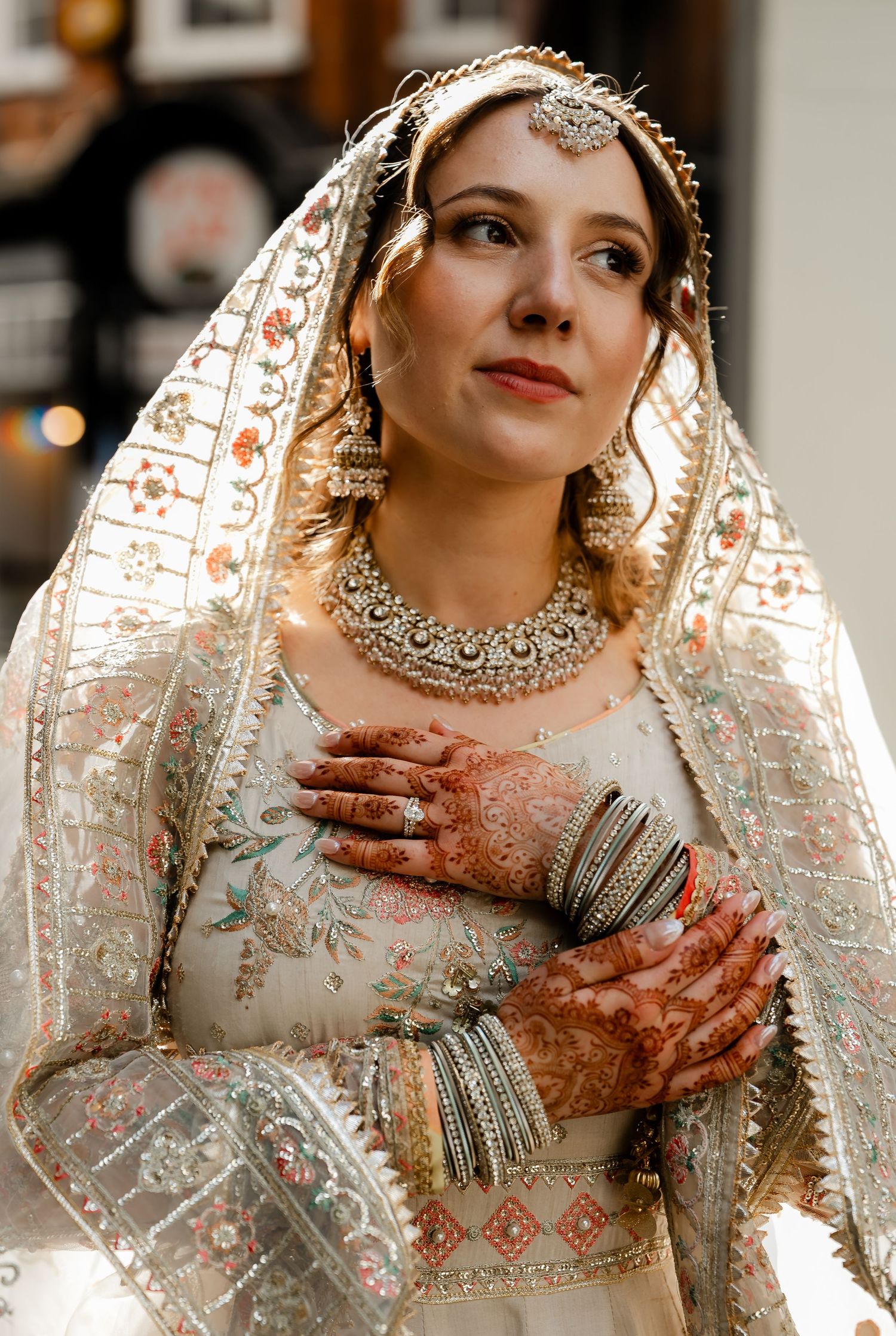 Beautiful South Asian bride in ivory lehenga with intricate henna hands, maang tikka, and statement necklace.