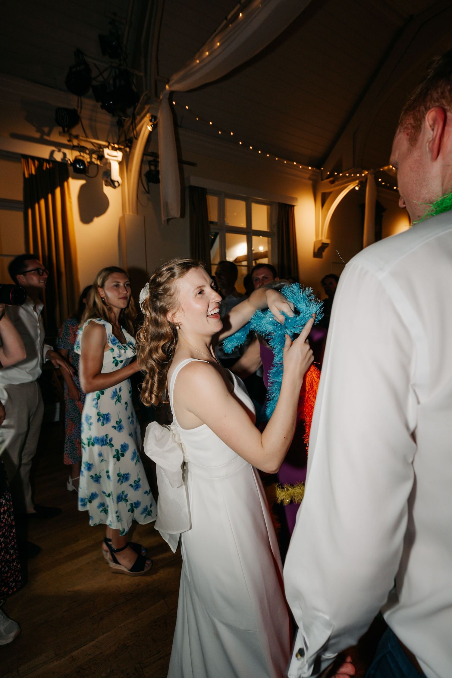Young girl in white dress dancing joyfully at a wedding reception with guests celebrating in background.