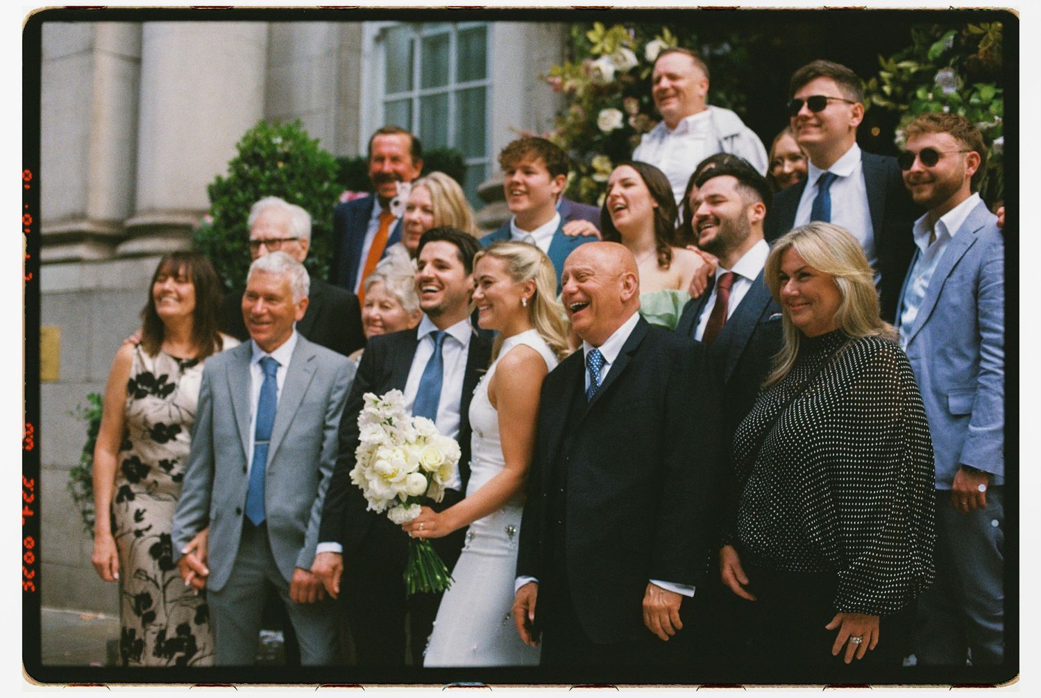 Wedding party group portrait with bride and groom outside a grand historic building.
