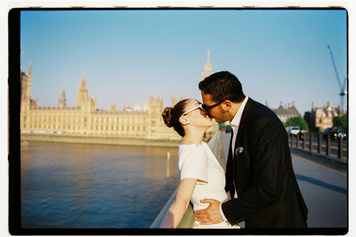 Wedding couple kissing on bridge overlooking the River Thames and Houses of Parliament in London.