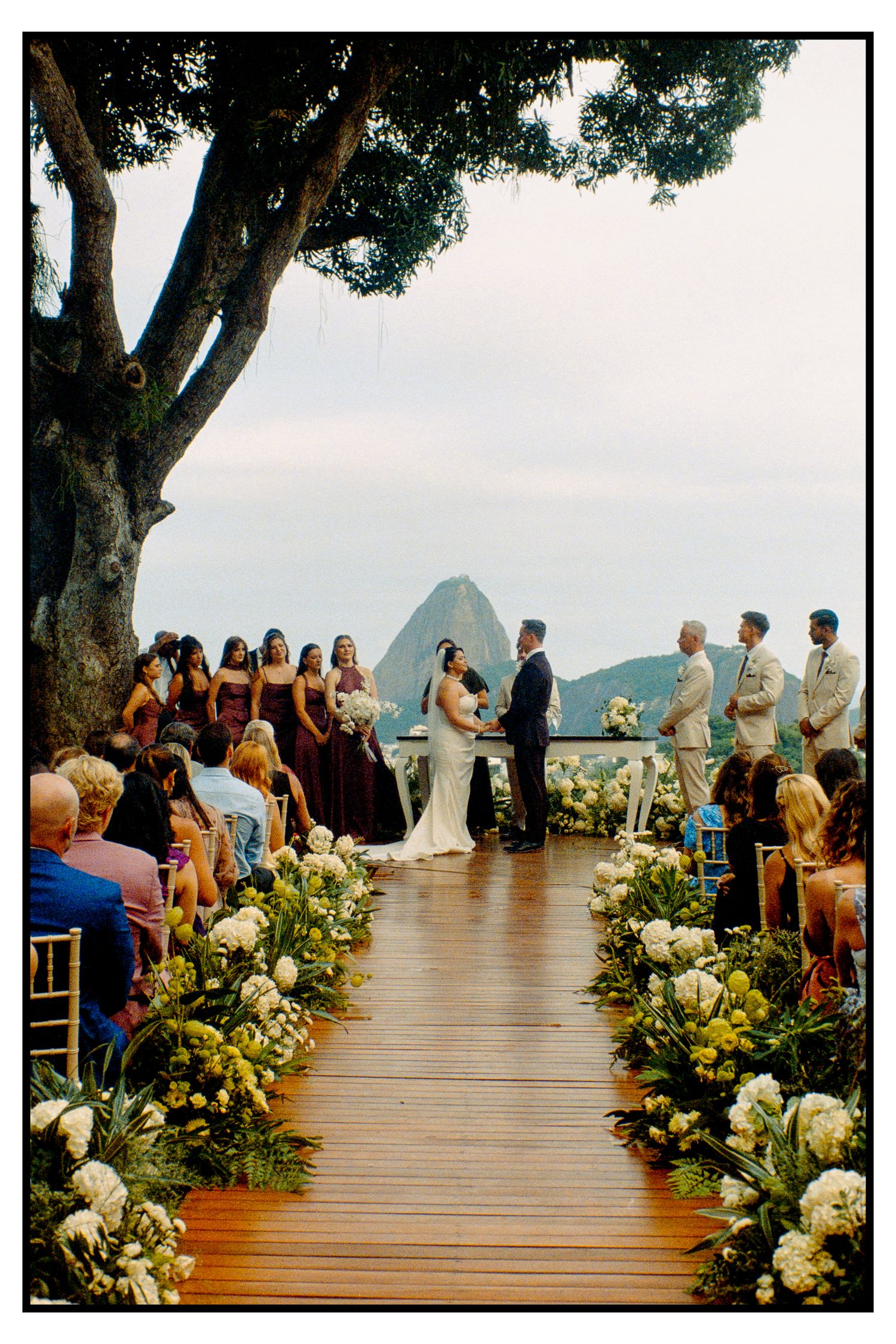 Stunning outdoor wedding ceremony aisle lined with white flowers, Sugarloaf Mountain visible in background.