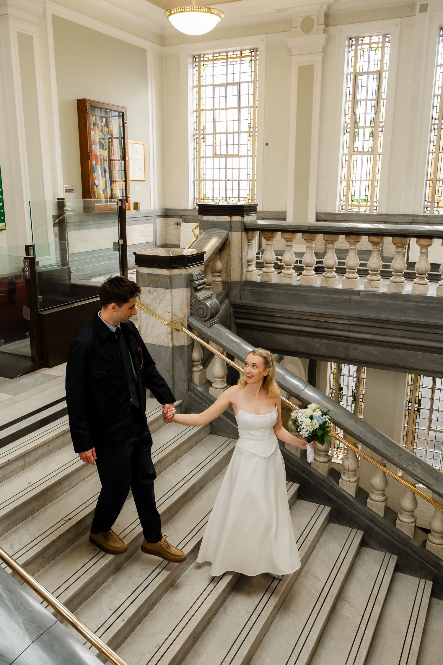 Bride and groom holding hands walking up elegant marble staircase in a grand wedding venue.