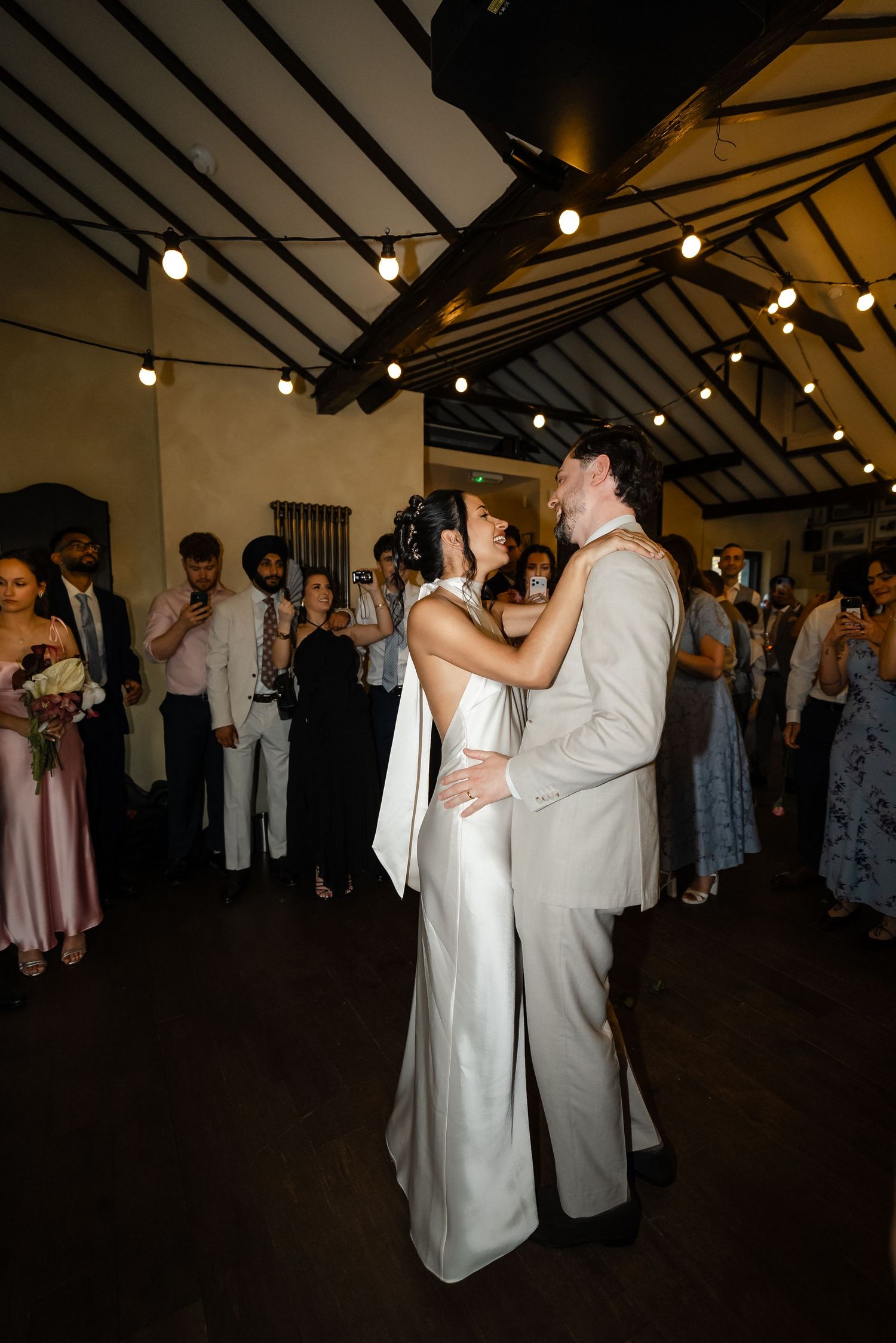 Bride and groom sharing intimate first dance surrounded by guests at romantic wedding reception.