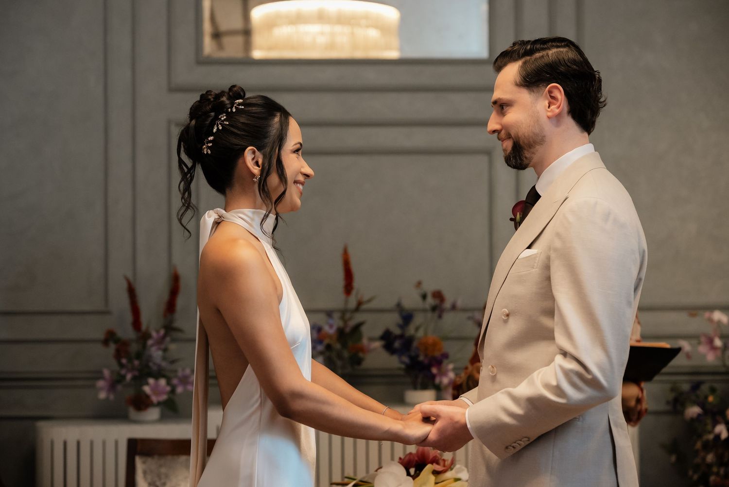 Bride and groom holding hands at intimate wedding ceremony, bride in halter neck dress and groom in beige suit.