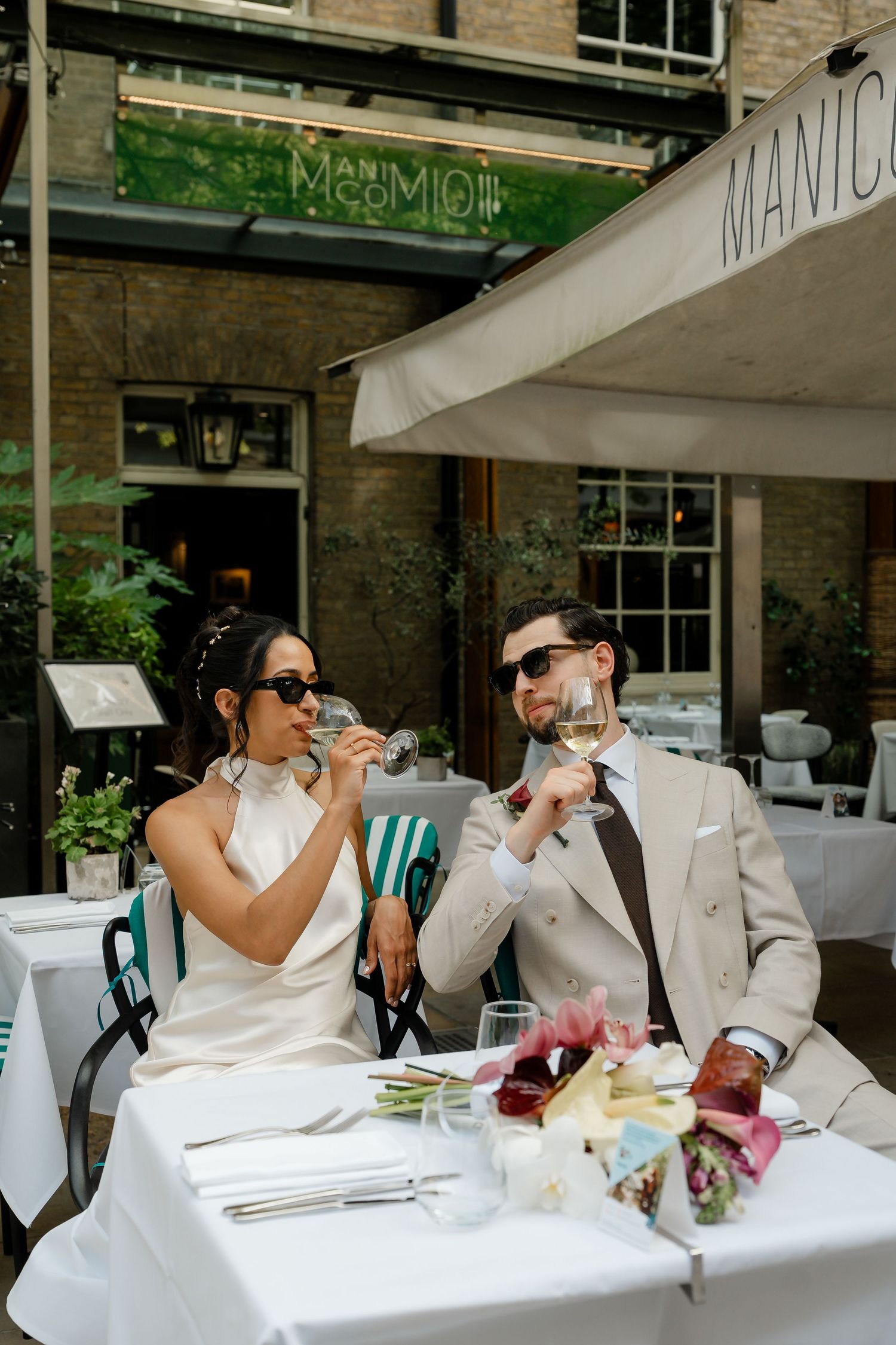 Bride and groom toasting with white wine at outdoor restaurant table at Manio during wedding reception.