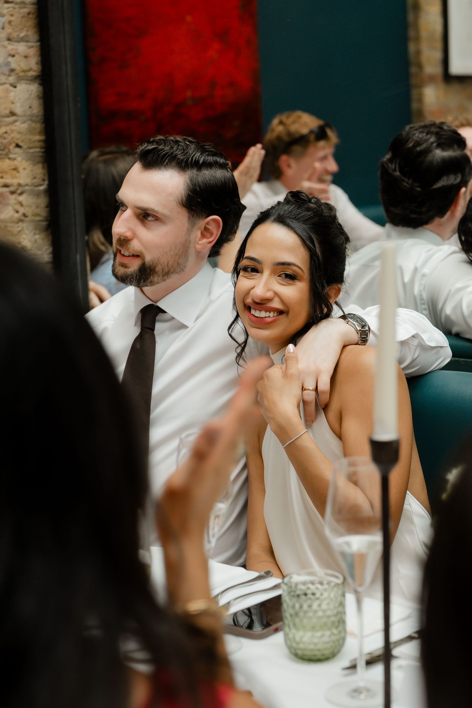 Smiling bride leaning on groom's shoulder at elegant wedding reception dinner.