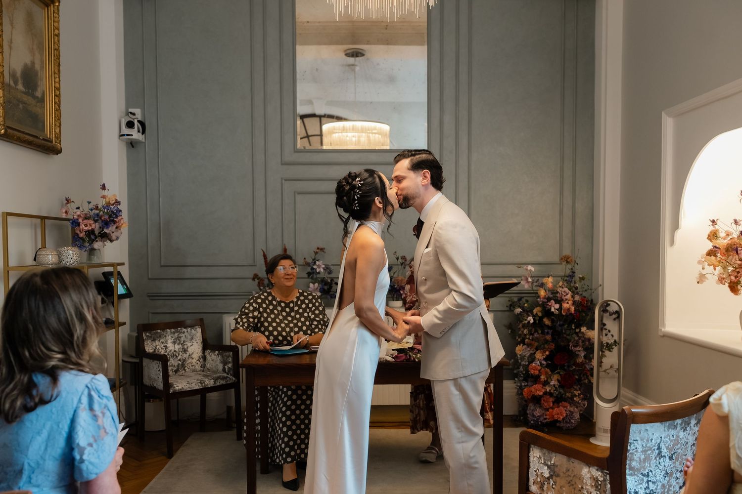 Bride and groom share their first kiss at the altar during an intimate wedding ceremony with seated guests.