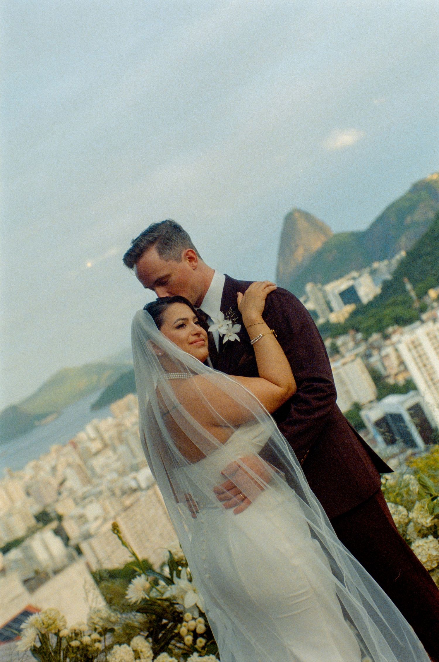 Bride and groom embrace on rooftop with Rio de Janeiro cityscape and Sugarloaf Mountain backdrop.