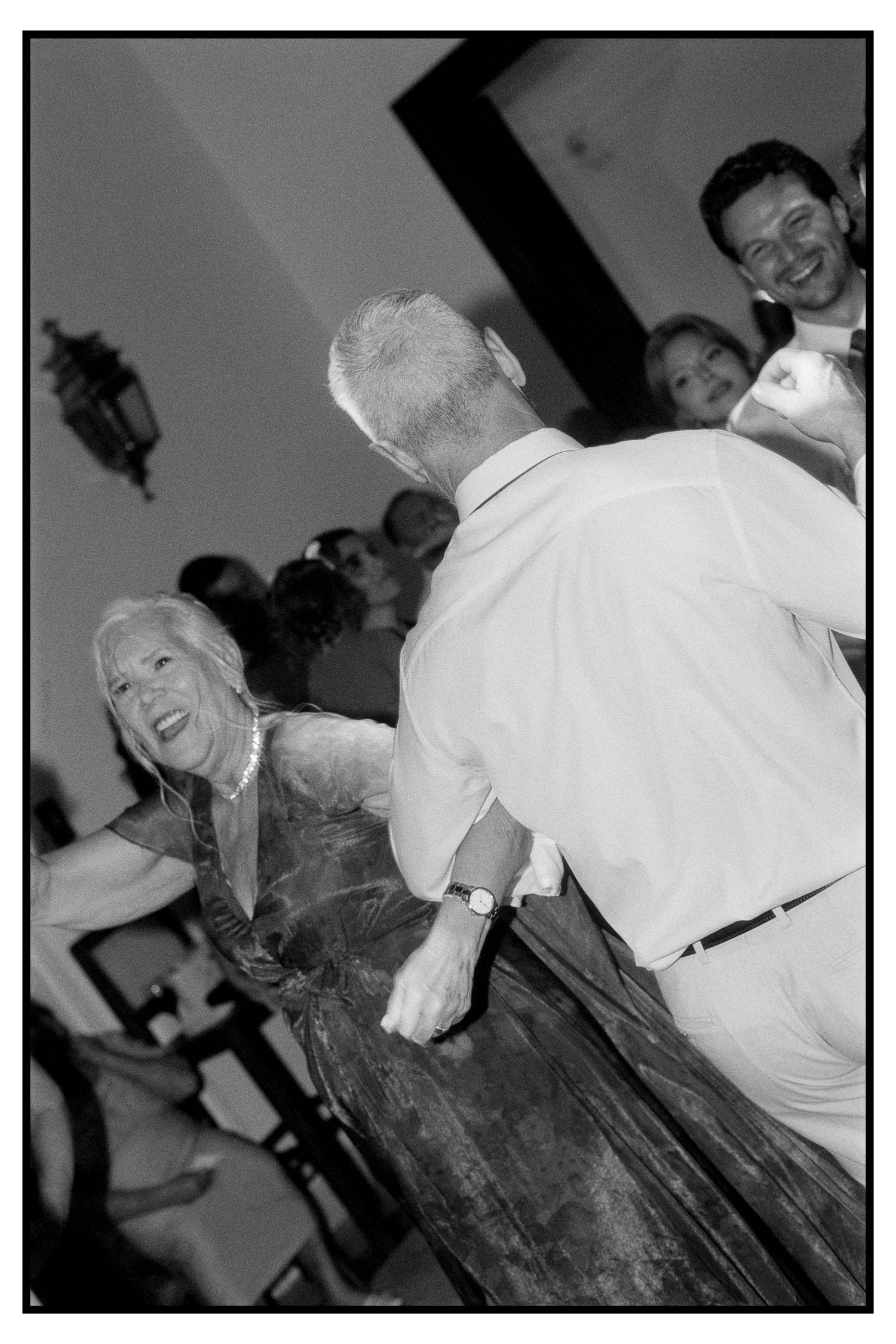Black and white photo of elegant older couple dancing joyfully at wedding reception.