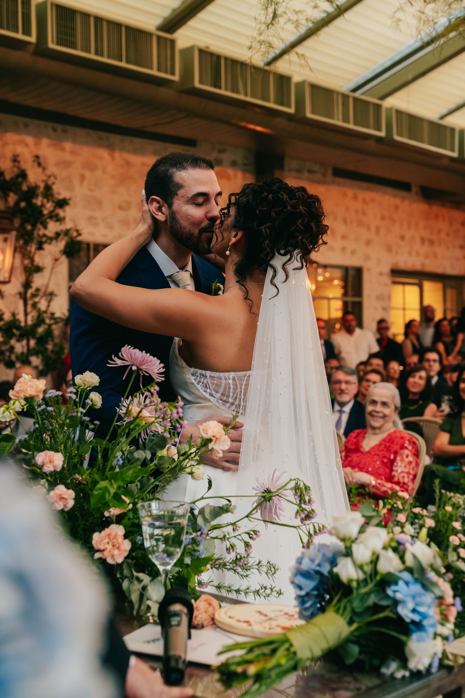 Bride and groom share their first kiss at the altar with guests watching in a rustic venue.