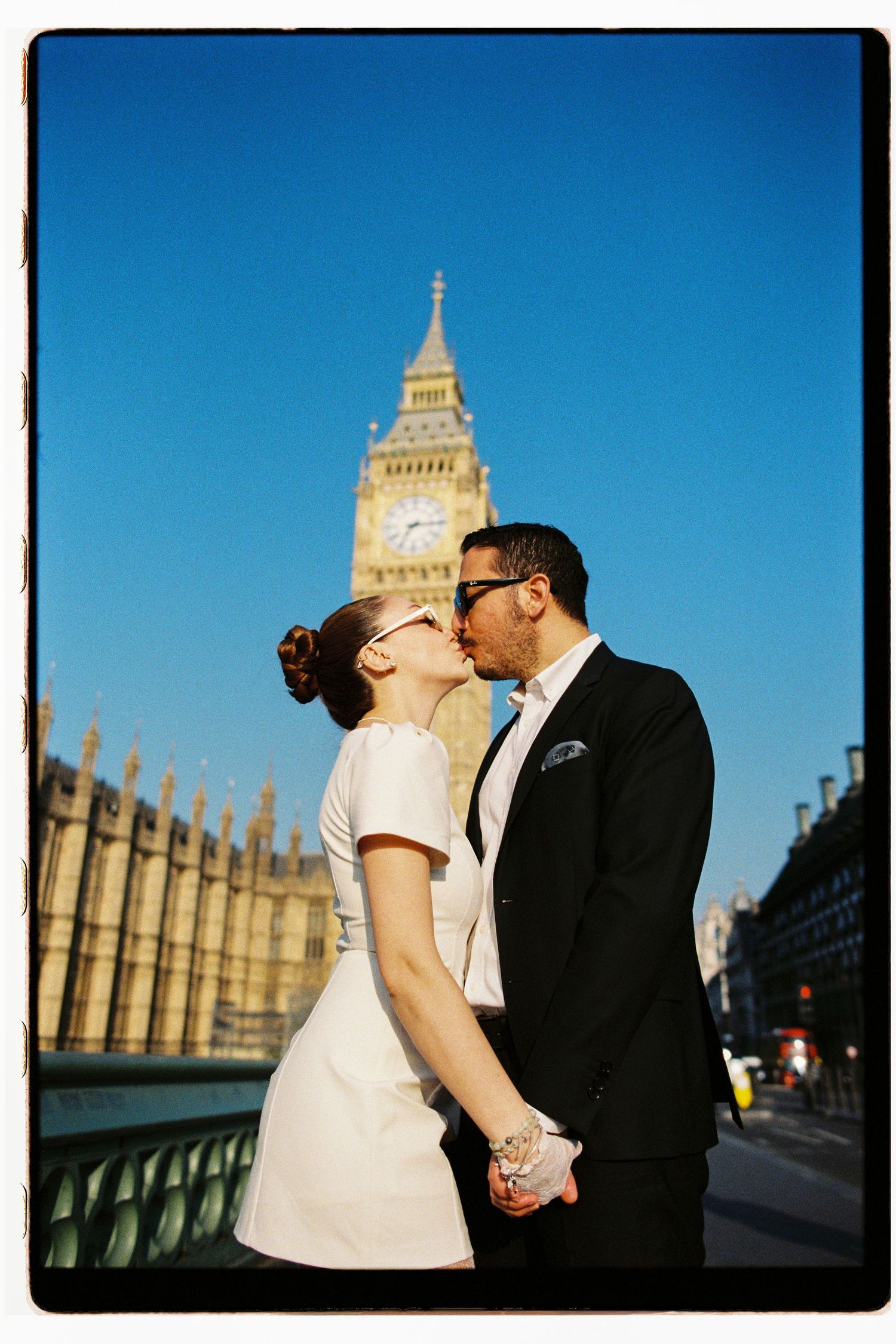 Bride and groom kissing on Westminster Bridge with Big Ben clock tower rising behind them.