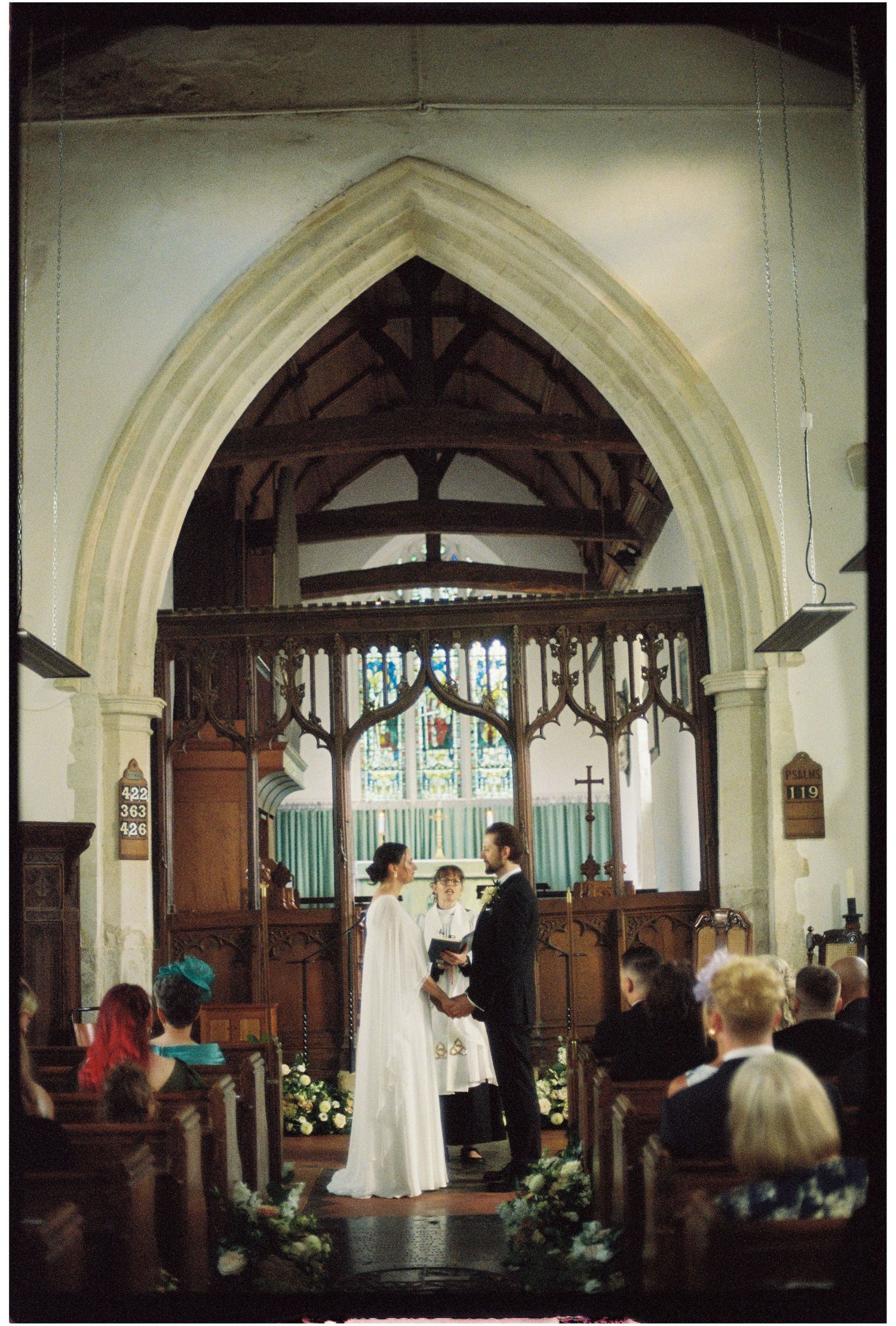 Bride and groom exchanging vows at the altar of a historic stone church with gothic arch and wooden rood screen.