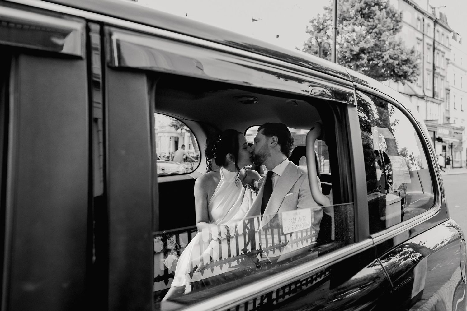 Black and white photo of bride and groom sharing intimate moment inside classic London black taxi cab.