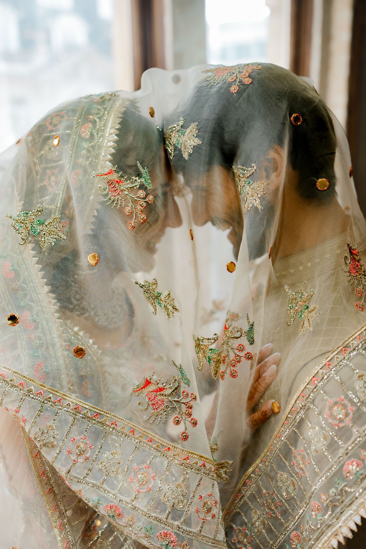 Close-up of intricate floral embroidery and mirror work on bride's sheer ivory dupatta veil at South Asian wedding.