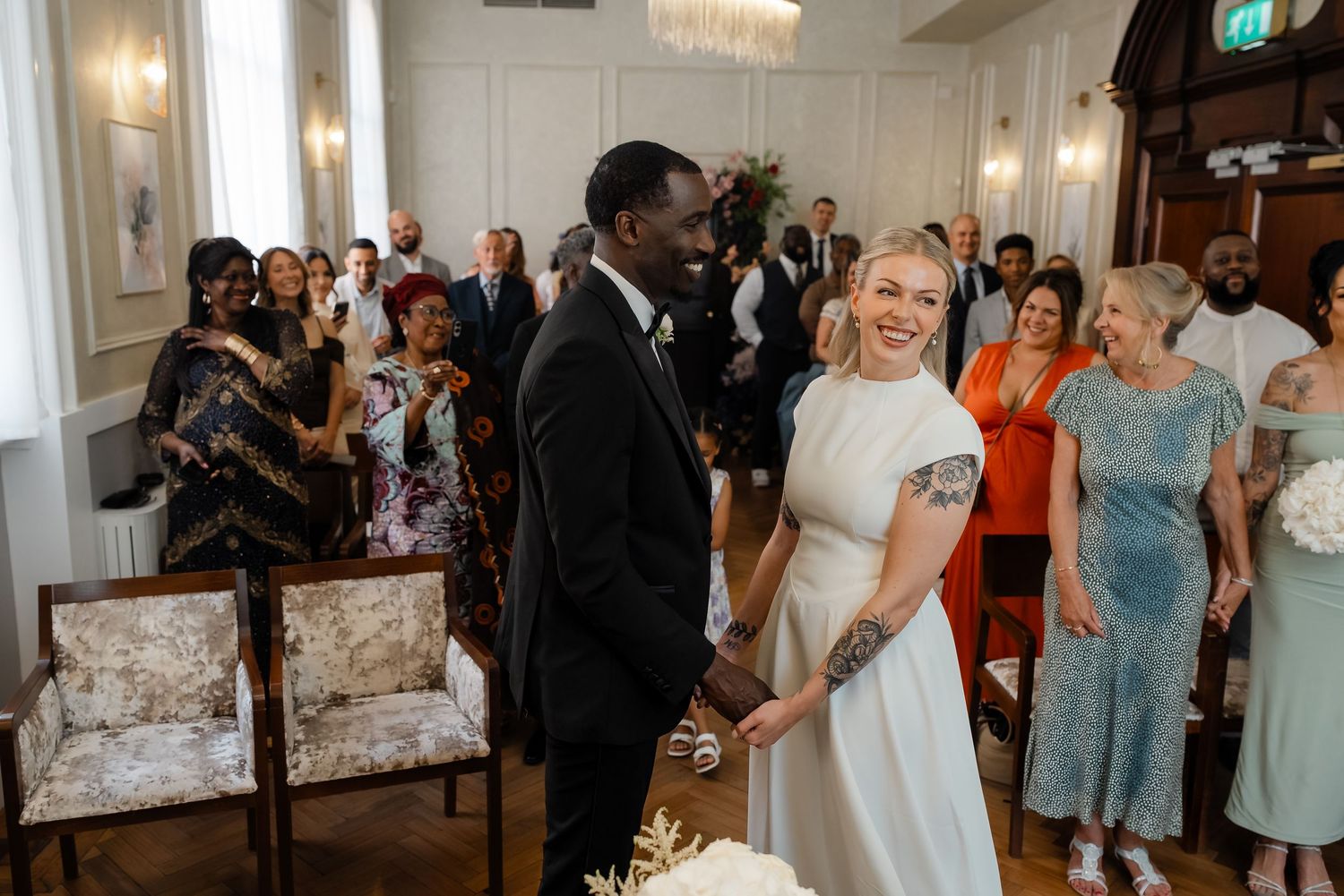 Smiling bride and groom holding hands at the altar with happy guests applauding behind them.