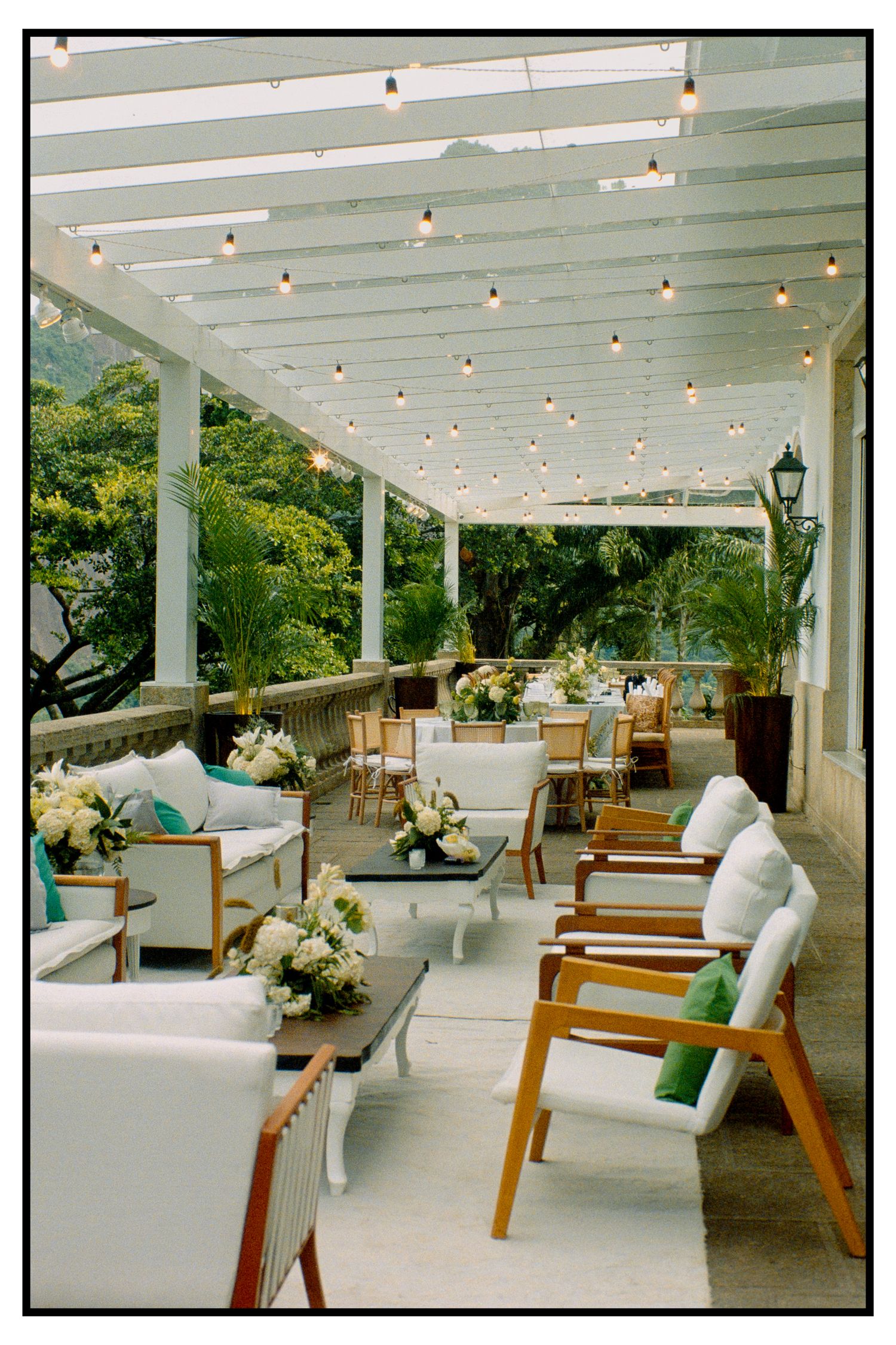 Elegant outdoor wedding reception terrace with white furniture, string lights, and lush tropical garden views.