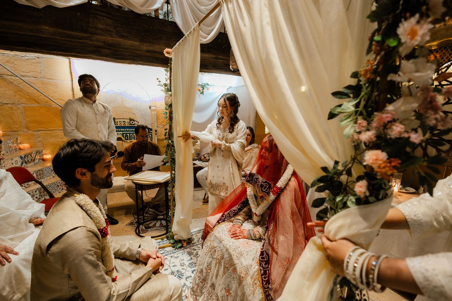 Bride and groom sharing intimate moment under white draped canopy during traditional South Asian wedding ceremony.