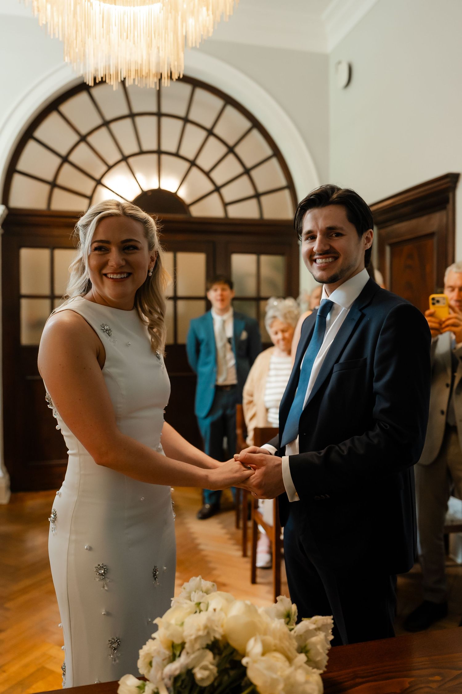 Smiling bride and groom hold hands during civil wedding ceremony in an elegant registry office.