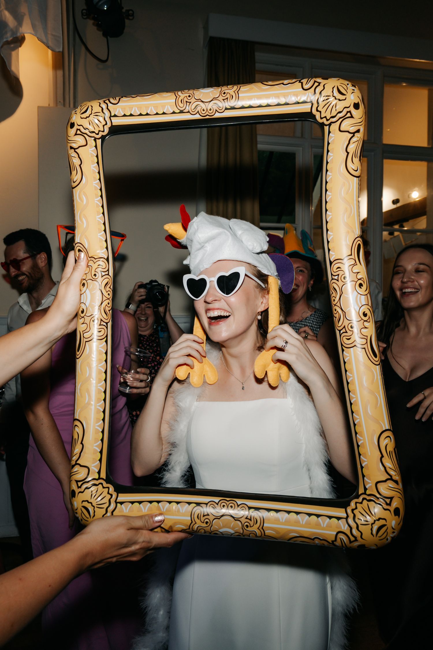 Bride wearing heart sunglasses and chef hat poses inside a decorative golden picture frame.
