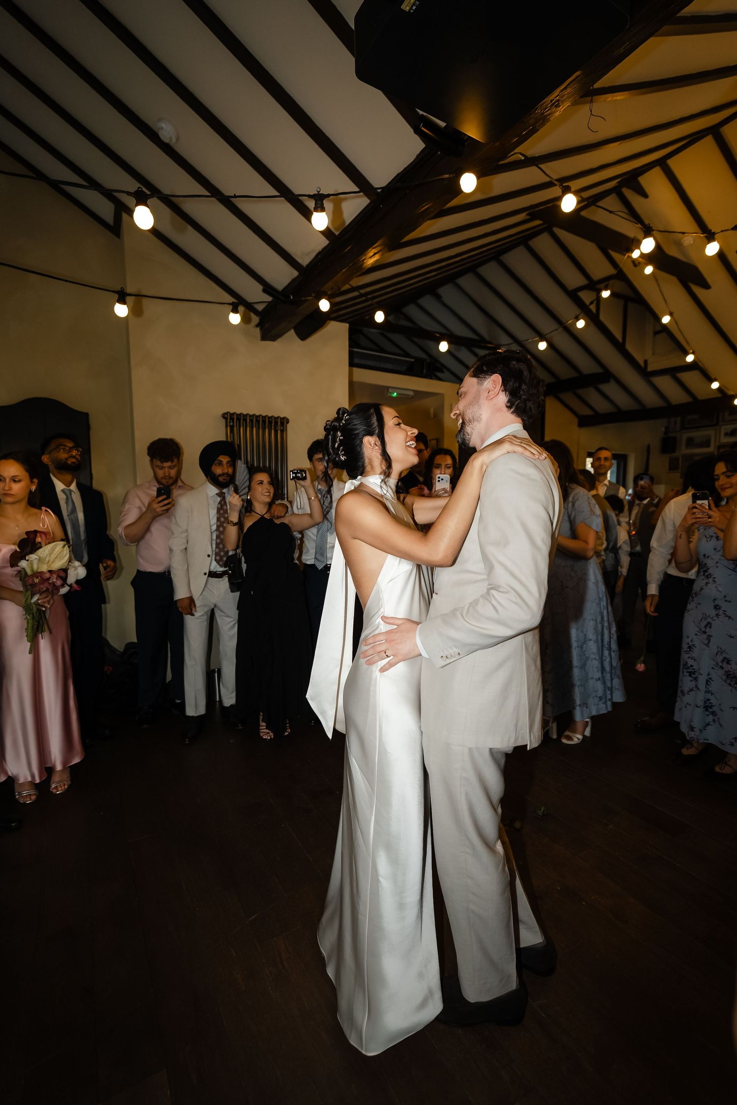 Bride and groom share their first dance surrounded by guests under warm string lights.