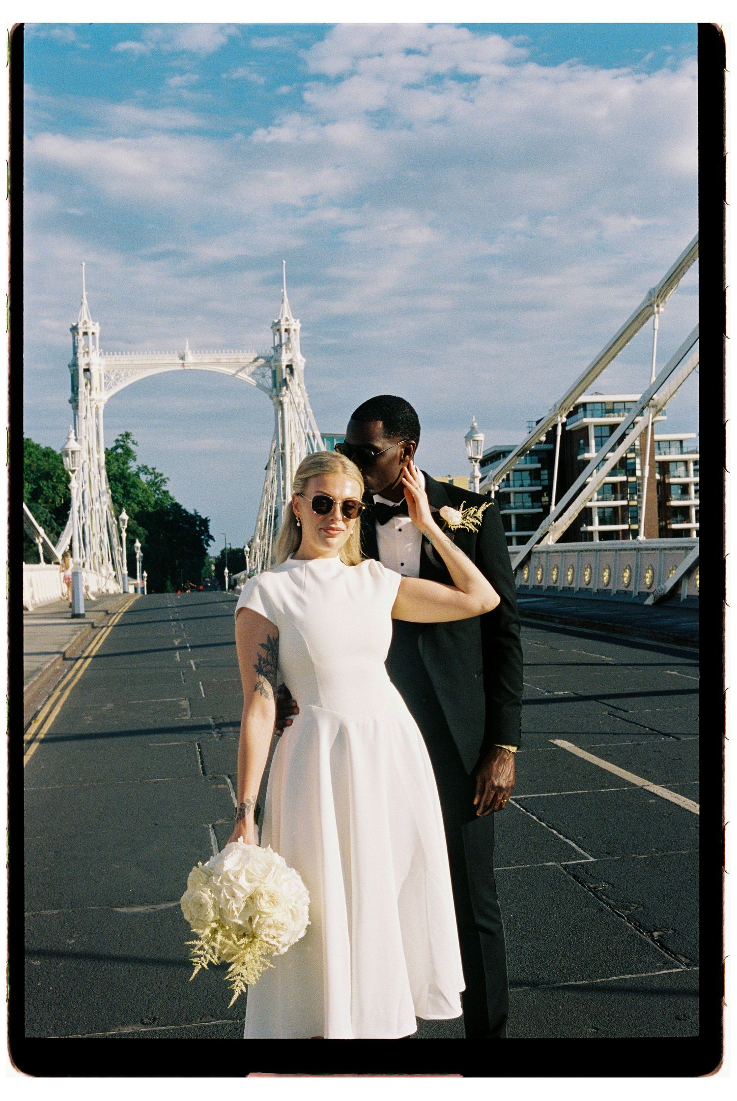 Bride and groom posing on Albert Bridge London, bride in white dress holding bouquet.