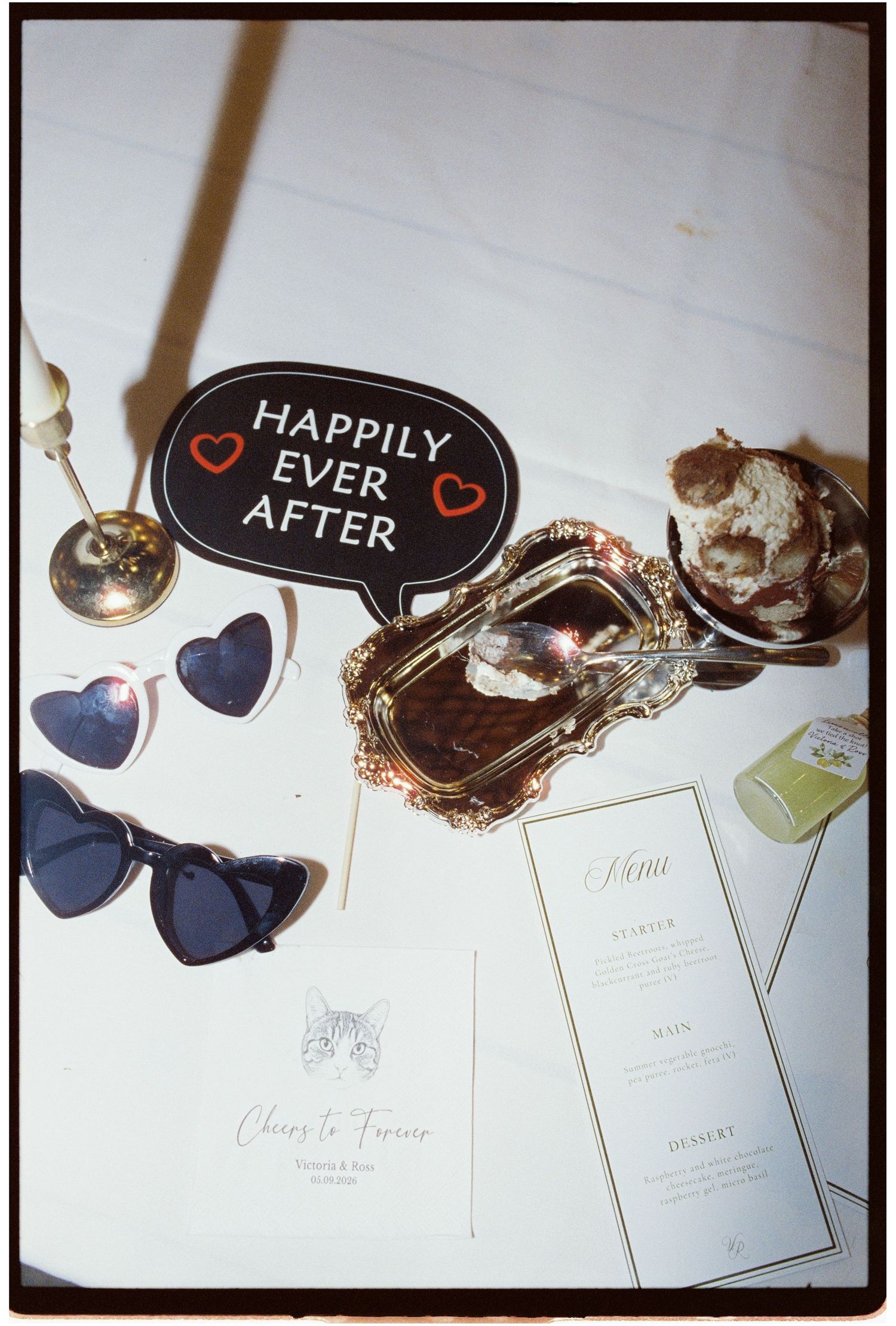 Wedding table display with Happily Ever After sign, heart sunglasses, menu cards, and dessert on silver tray.