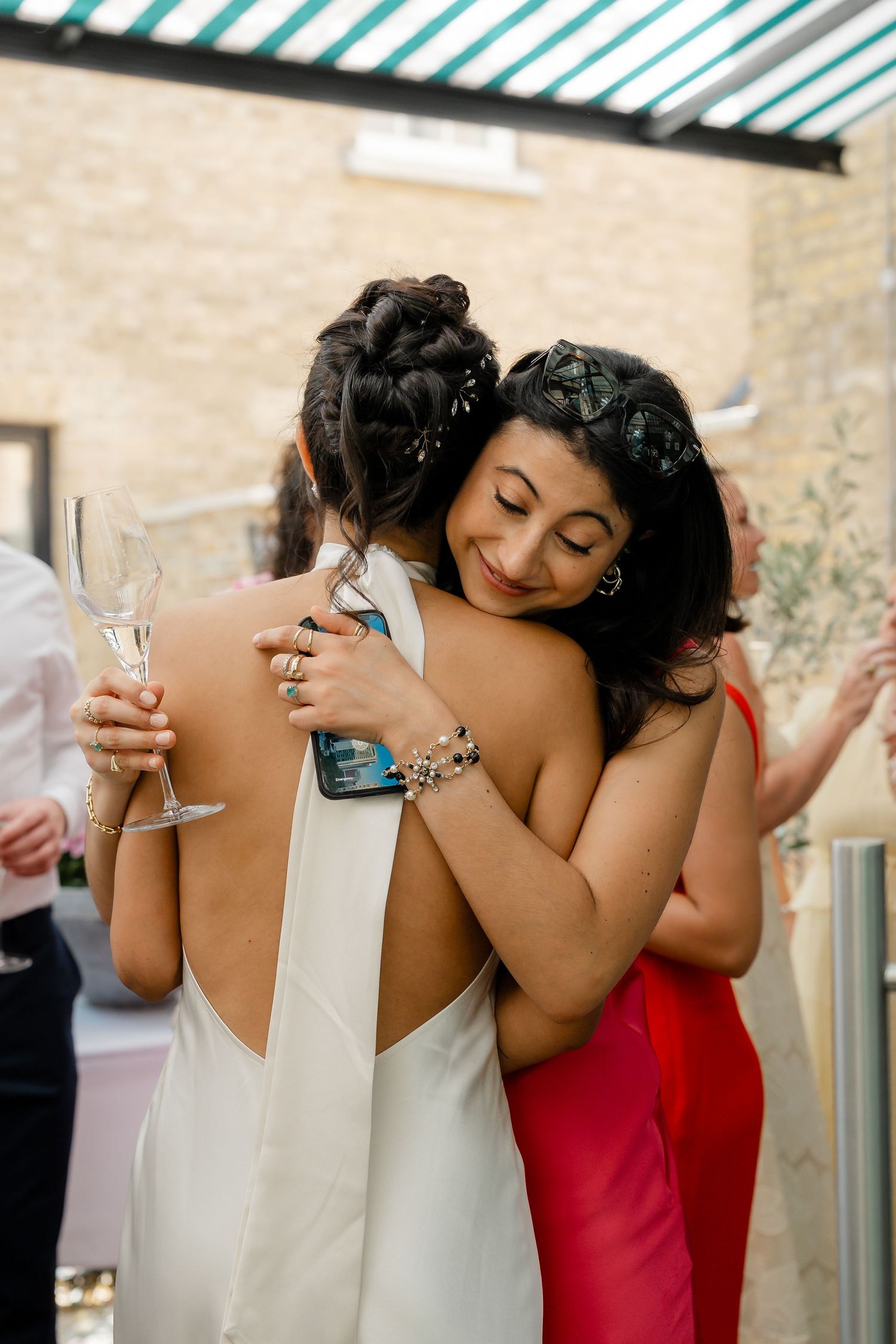 Bride and female guest sharing a warm embrace during an outdoor wedding reception celebration.