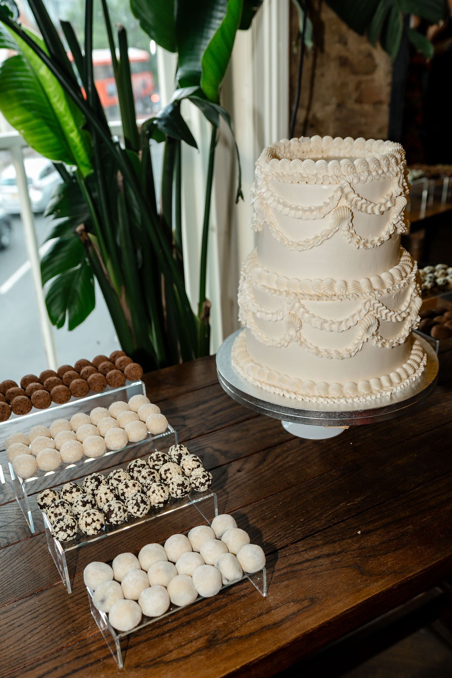 Elegant three-tier white wedding cake with piped swag details displayed beside chocolate and white cake pops.