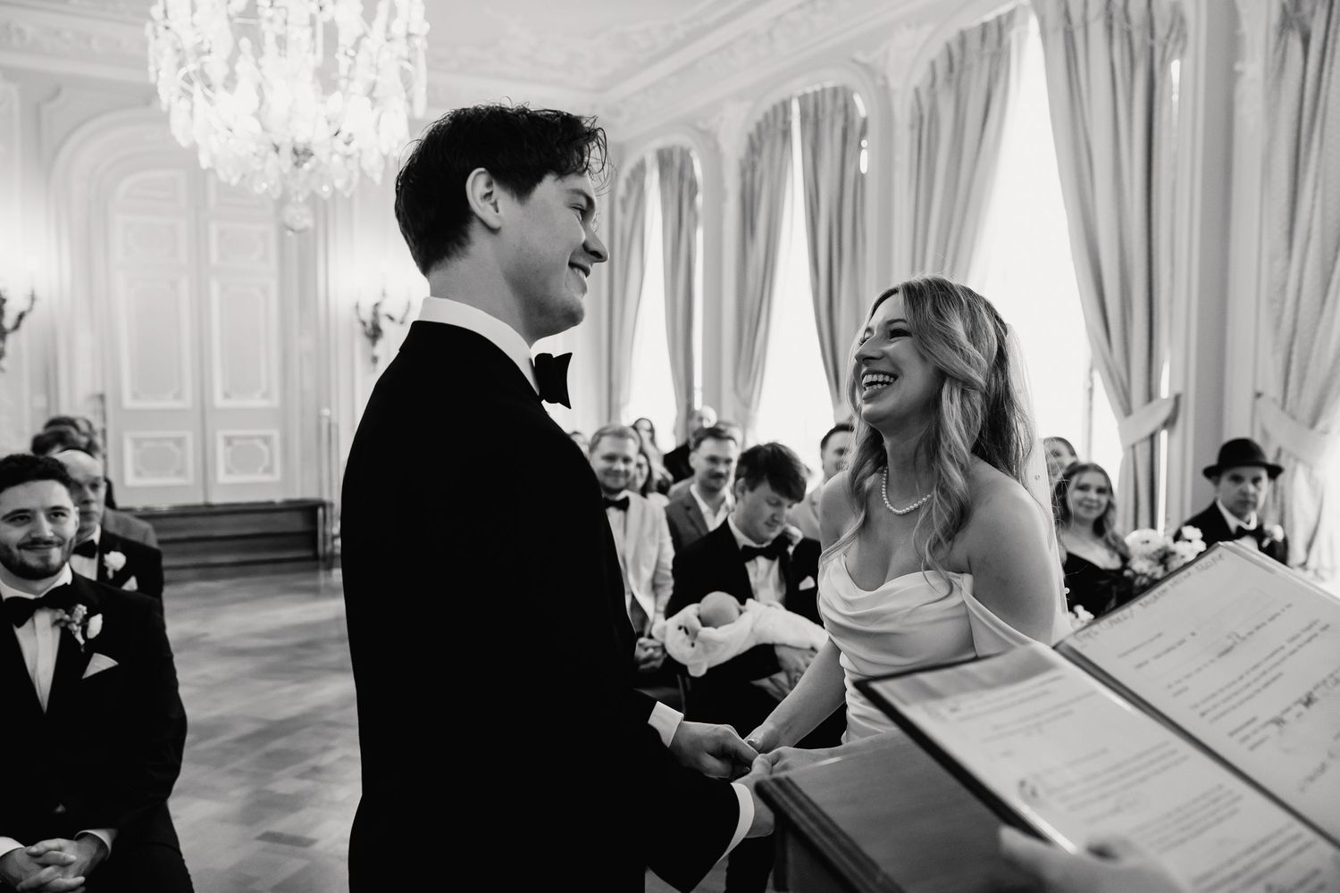 Black and white photo of joyful bride and groom laughing together during wedding ceremony.