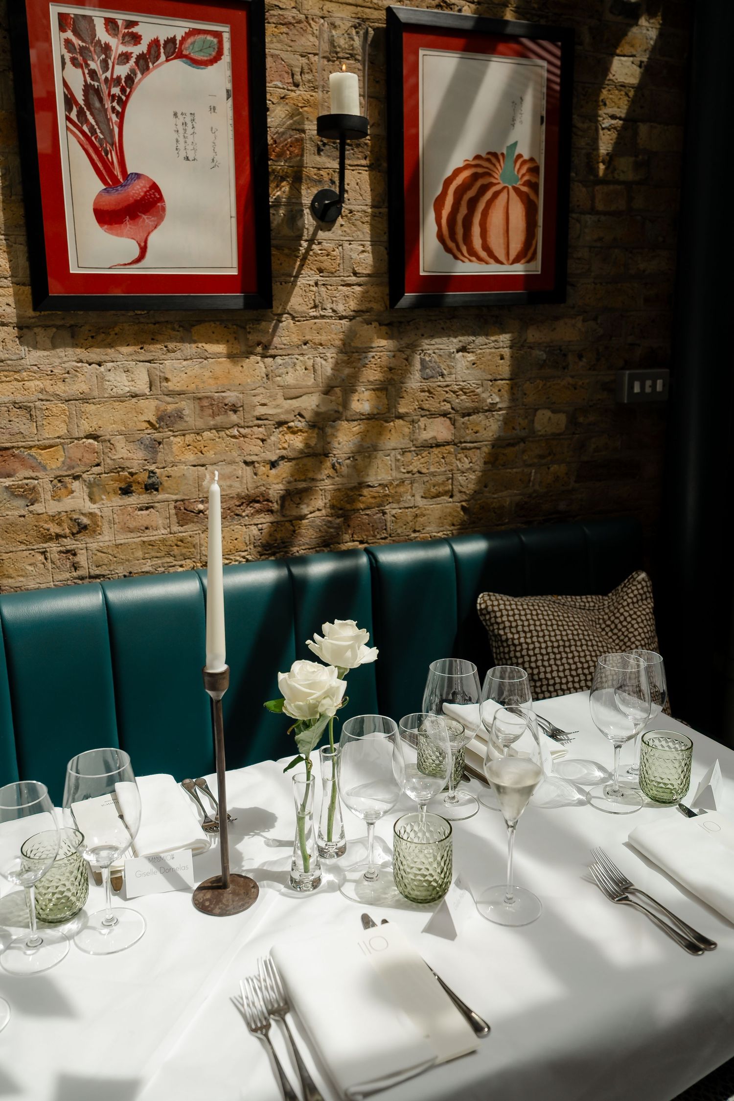 Elegant restaurant table set with white roses, candles, and glassware against a rustic brick wall.