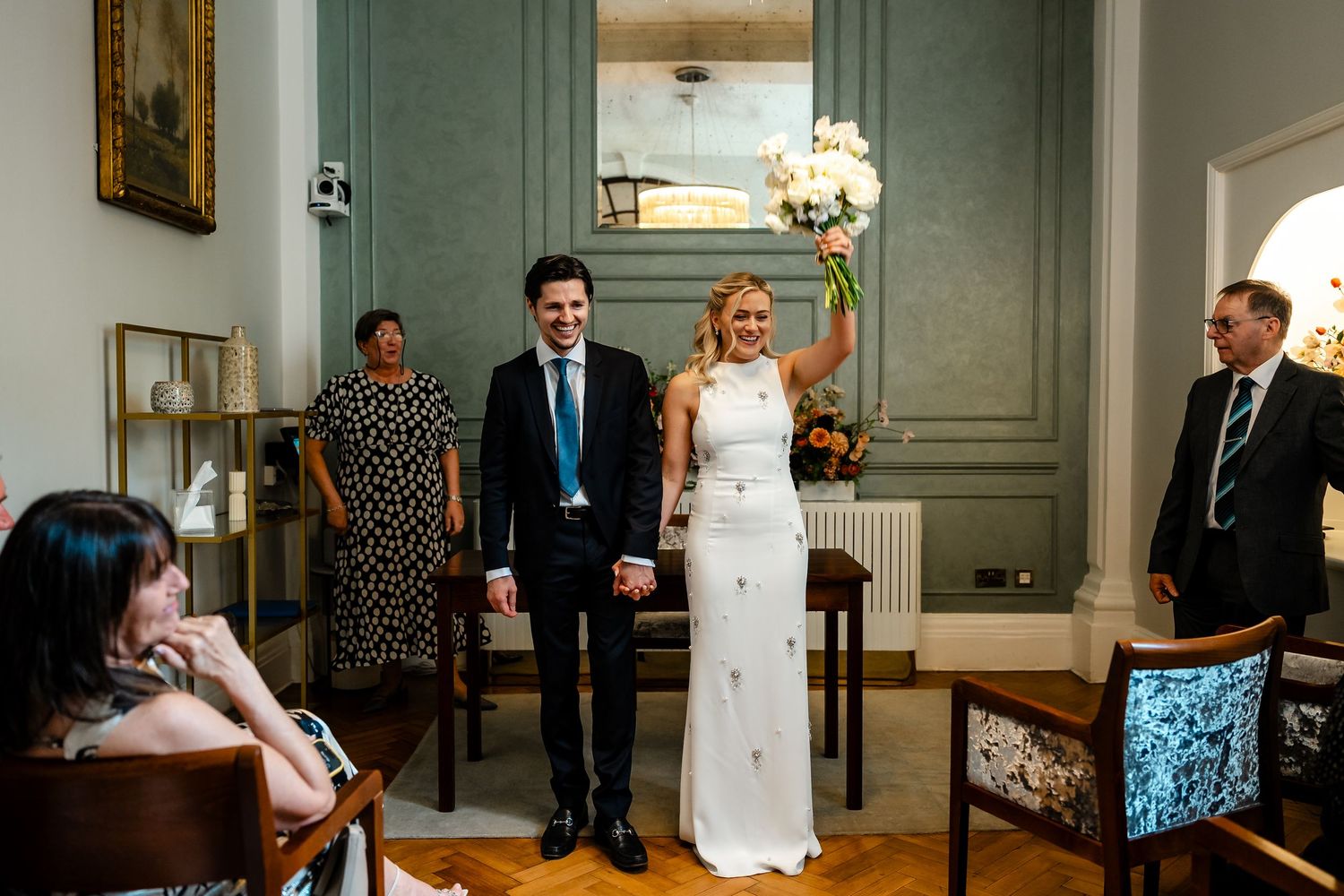 Newlyweds walk hand in hand as bride raises bouquet in celebration after ceremony.