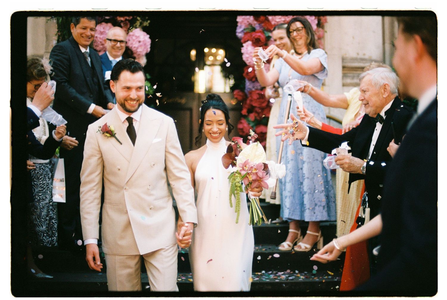 Newlyweds walking through confetti shower with guests celebrating at wedding exit.