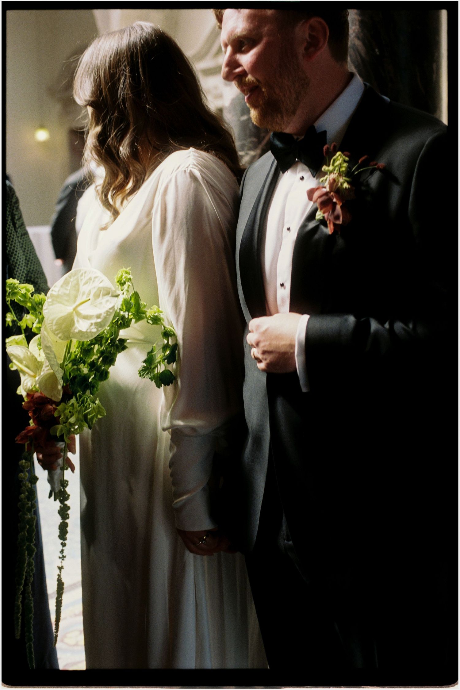 Bride in white gown and groom in tuxedo stand close during wedding ceremony.