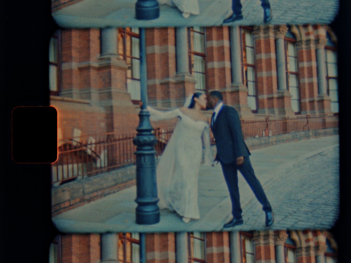 Bride and groom dancing near a lamp post outside a historic red brick building on their wedding day.