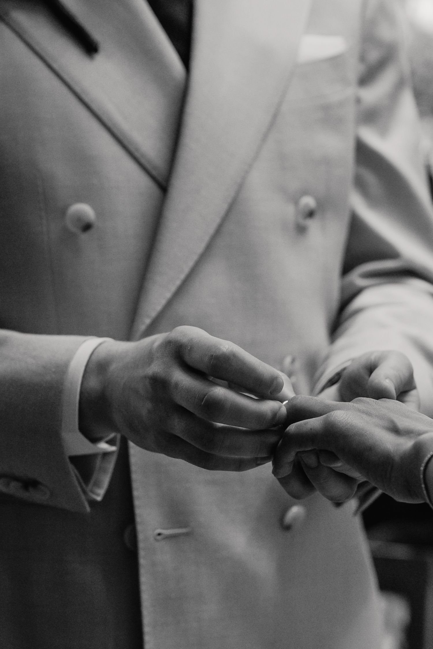 Close-up black and white photo of groom placing wedding ring on brides finger during ceremony.