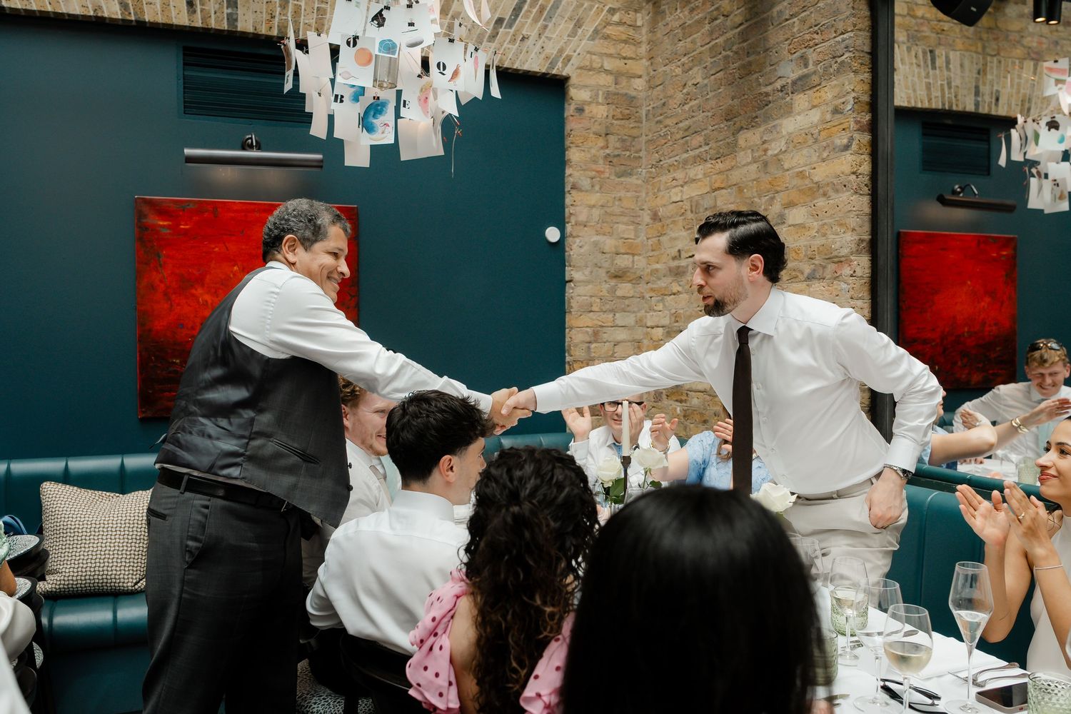 Two men shaking hands warmly across wedding reception dinner tables.