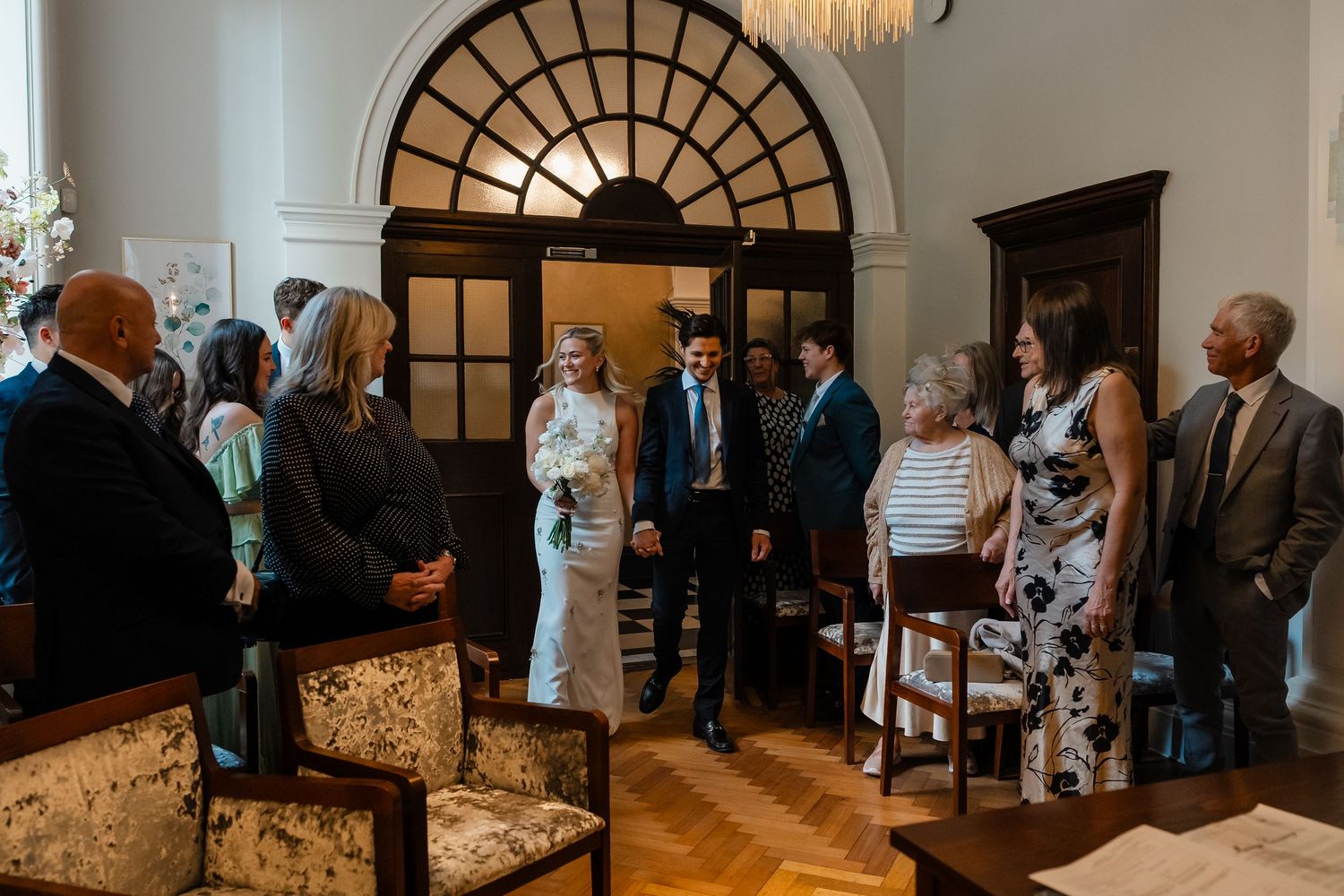Elegant wedding ceremony gathering in a grand room with guests standing around the bride and groom.